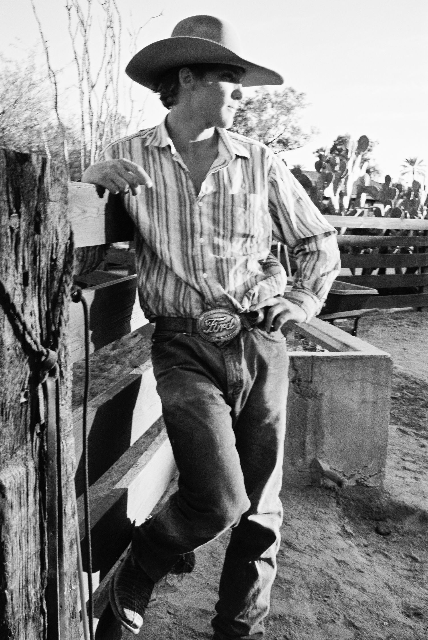 A black and white photograph shows cowboys in denim overalls and hats working outdoors on a ranch.