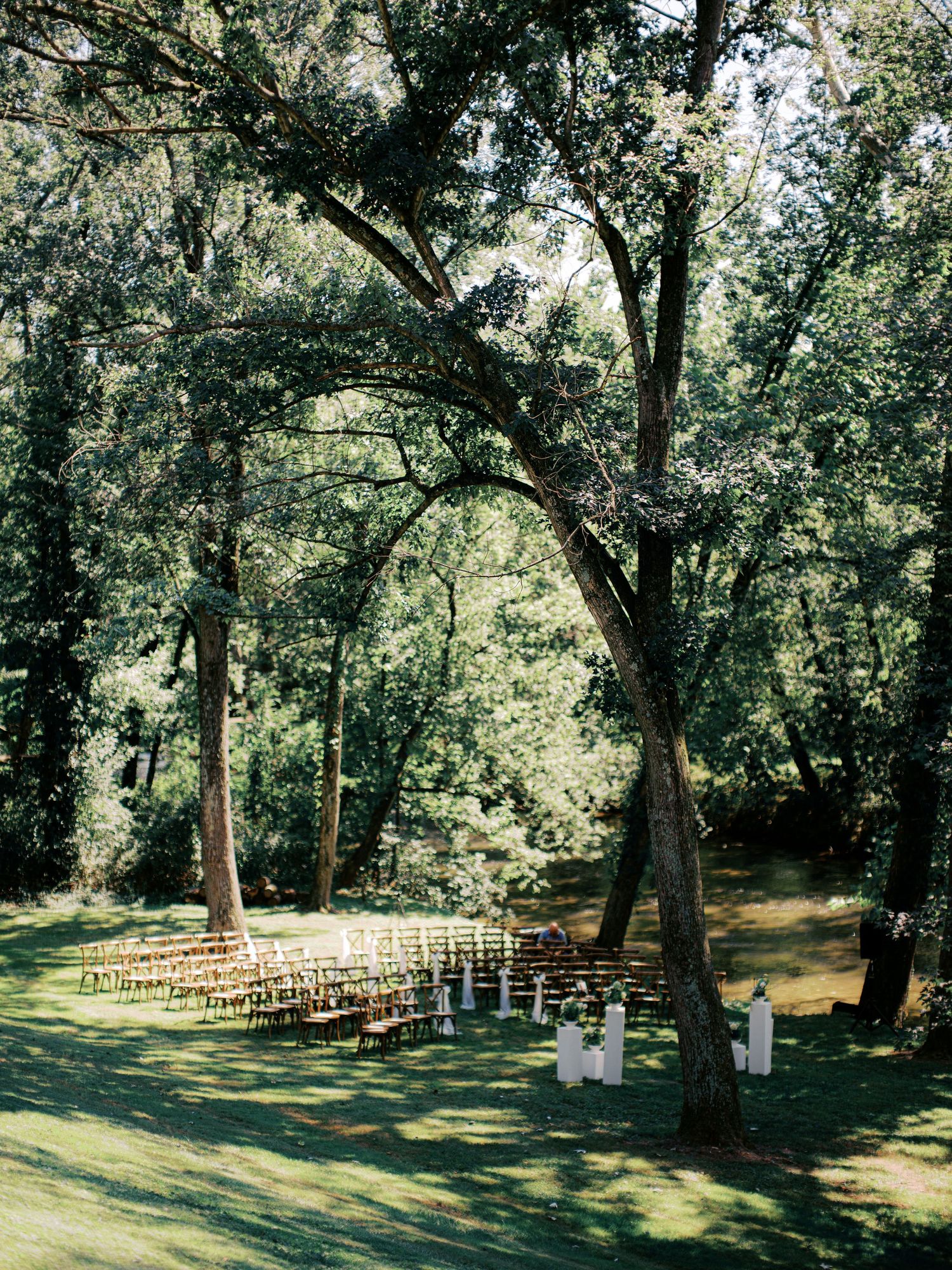 Rows of wooden chairs set up for an outdoor wedding ceremony under tall trees.