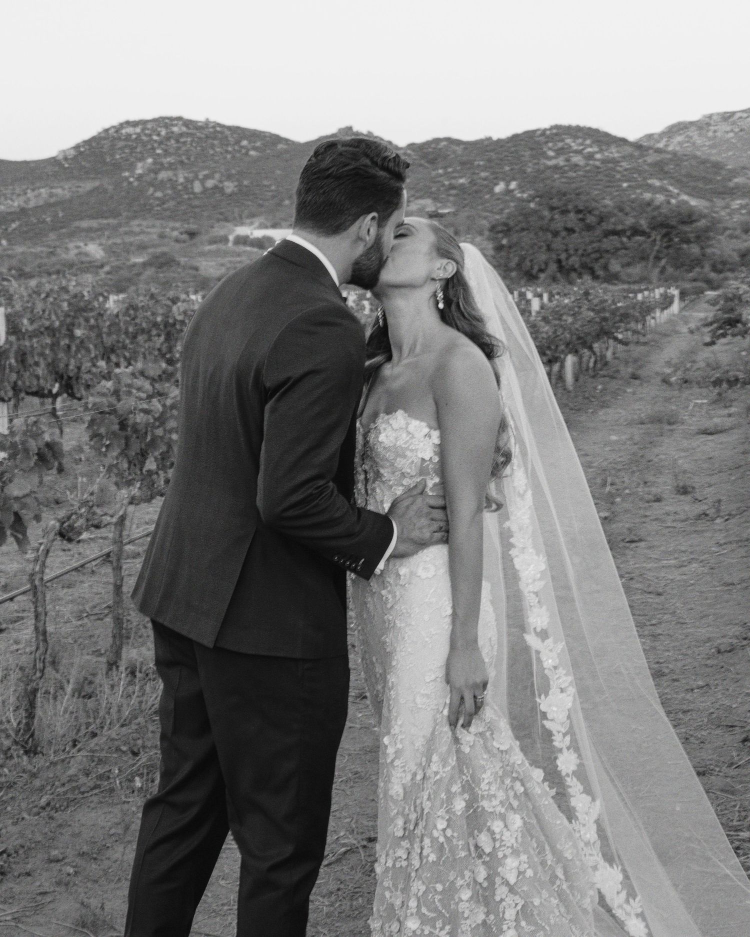 A romantic black and white photo series of a couple in wedding attire embracing outdoors in a desert landscape.