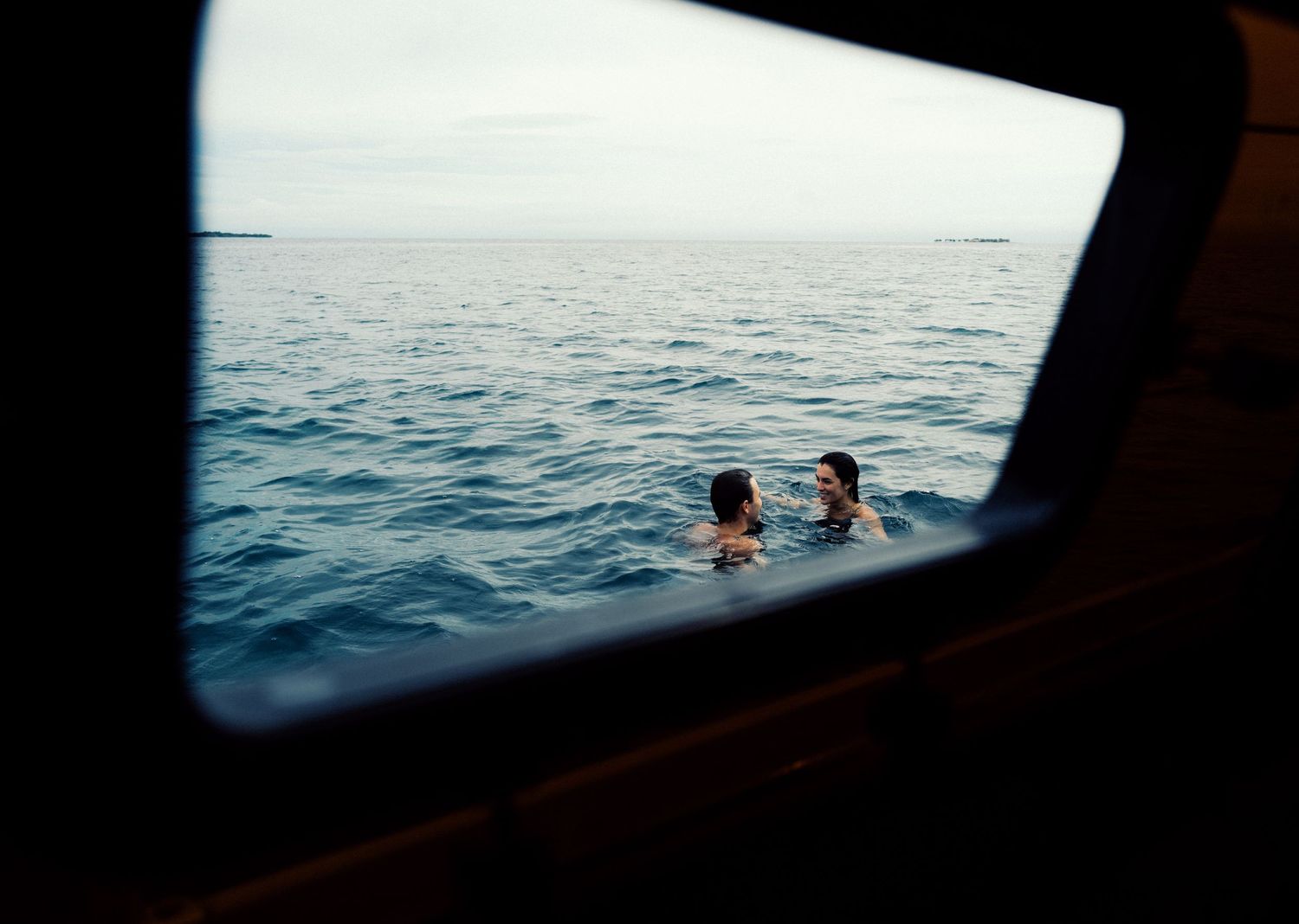 Swimmers floating in dark blue ocean water viewed through window frame at sunset.