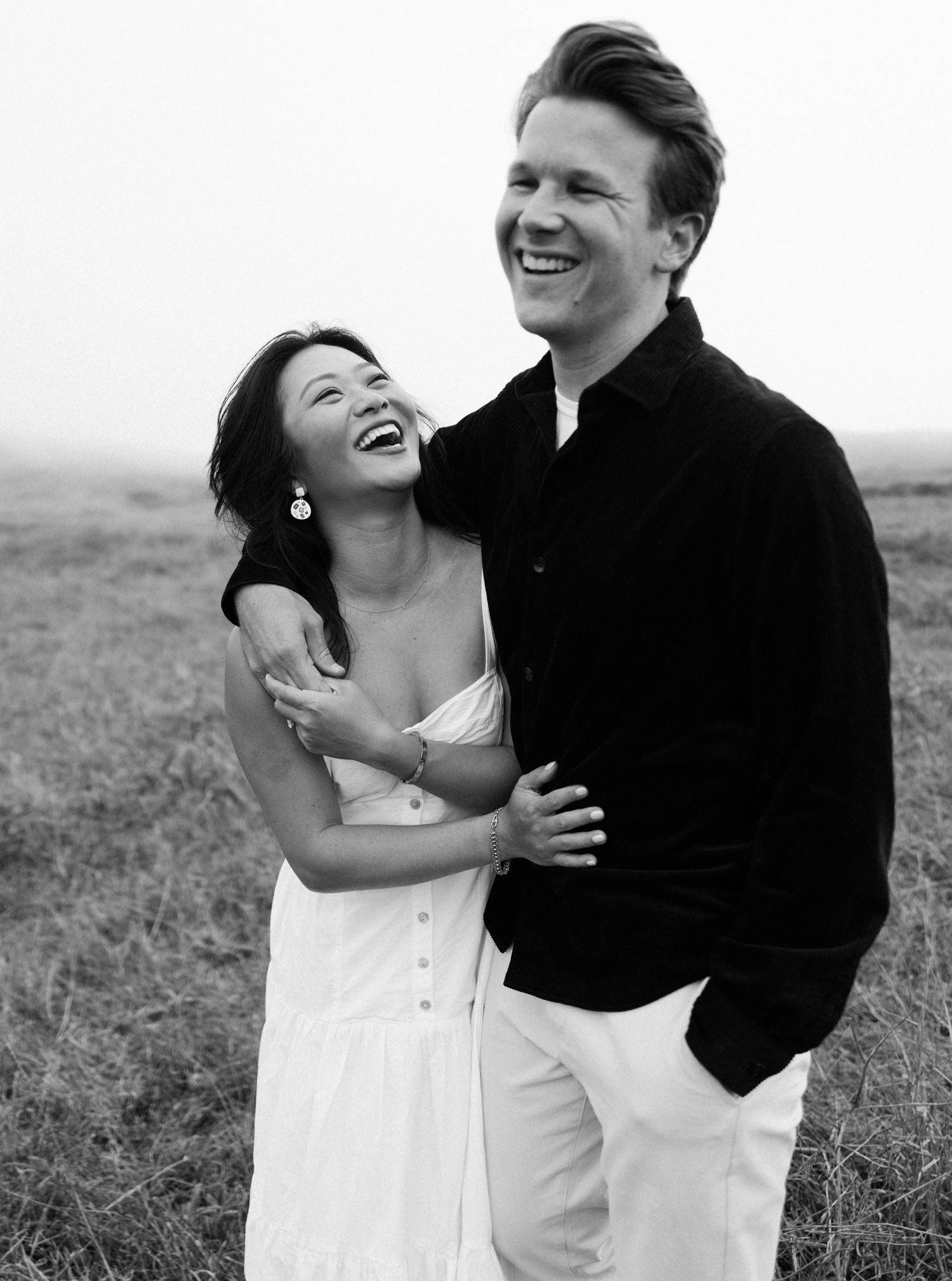 Black and white photo series of a couple laughing and embracing in a grassy field.