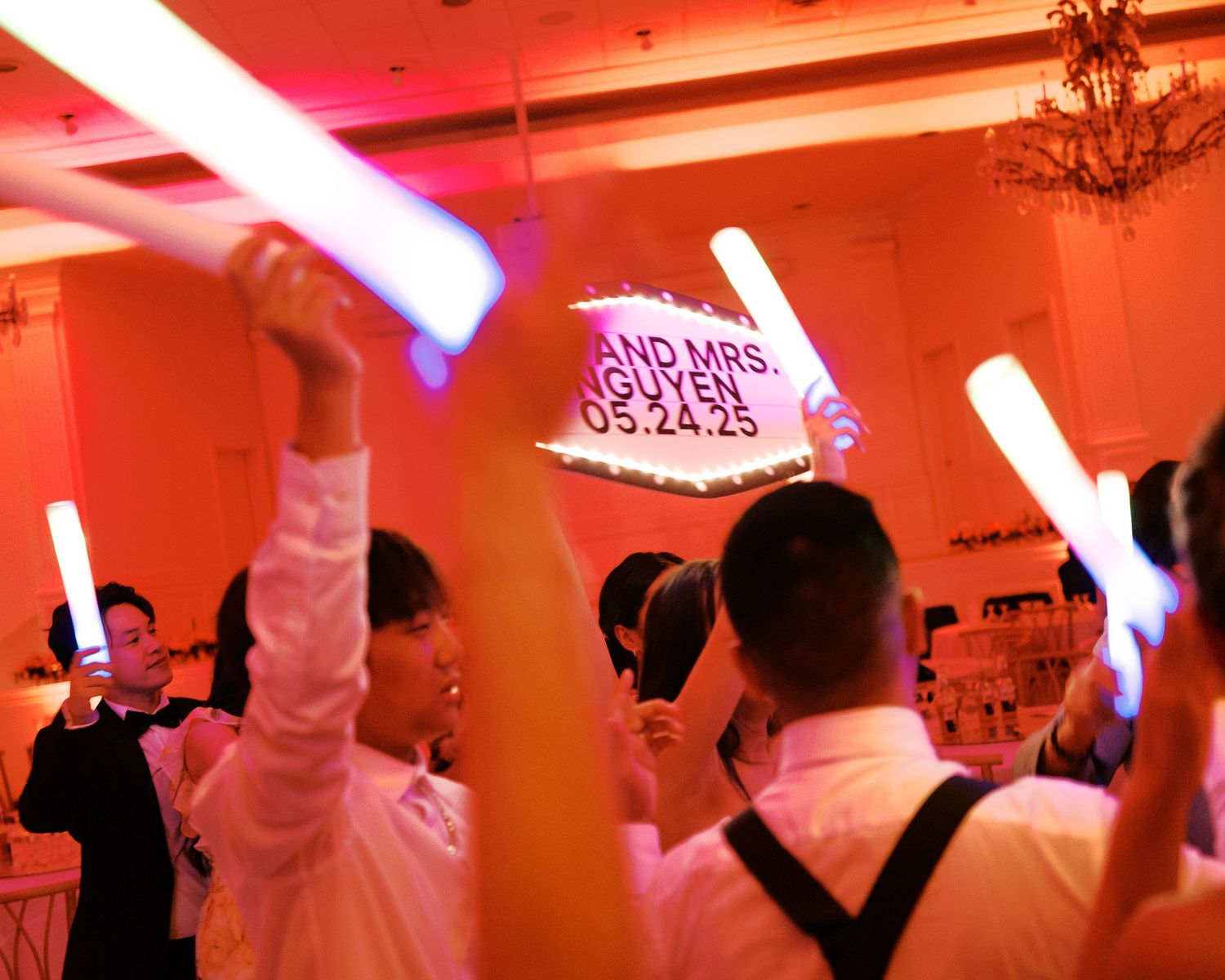 Wedding reception guests dancing and celebrating under red and purple lighting.