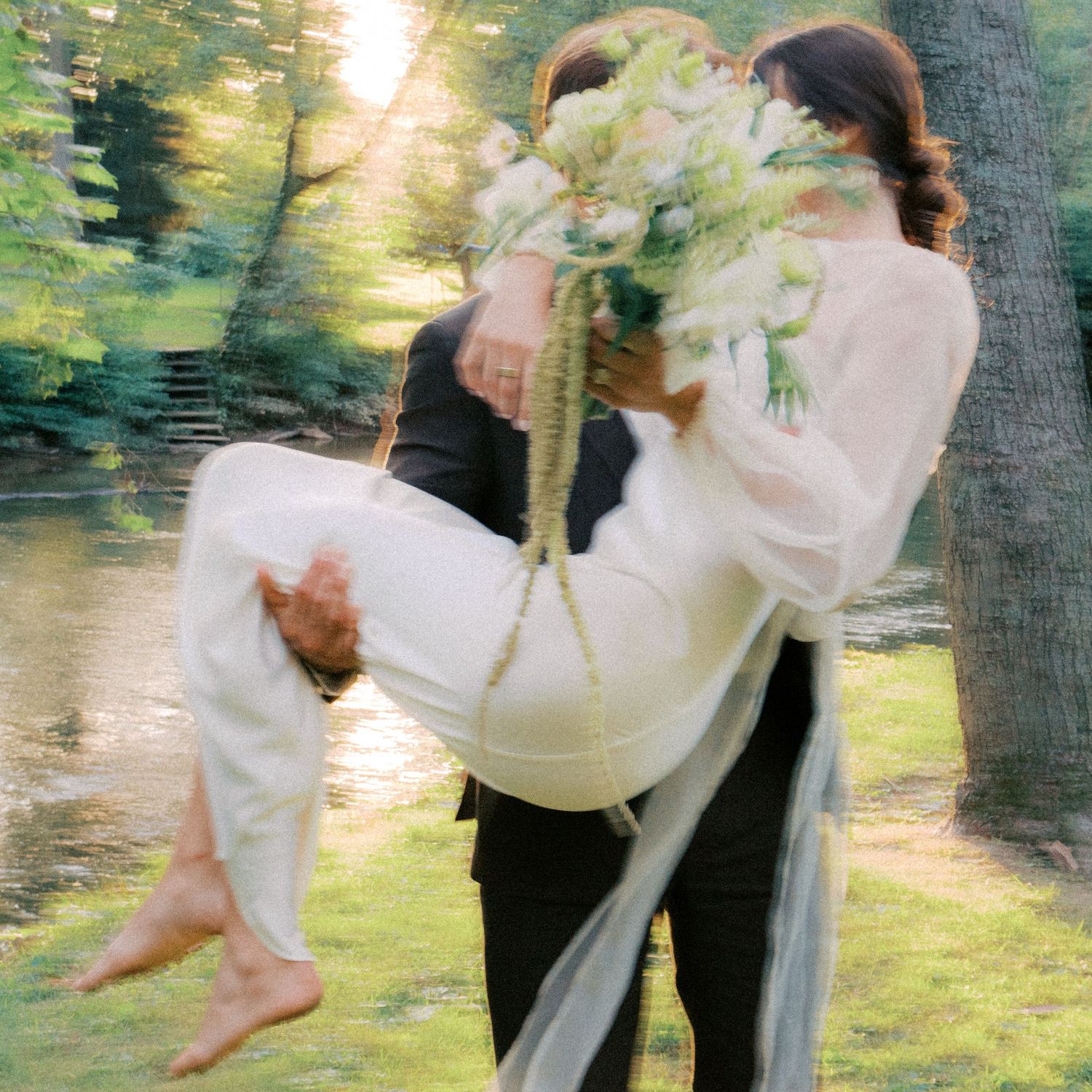 A couple dances together in a dreamy outdoor setting with soft sunlight filtering through trees.