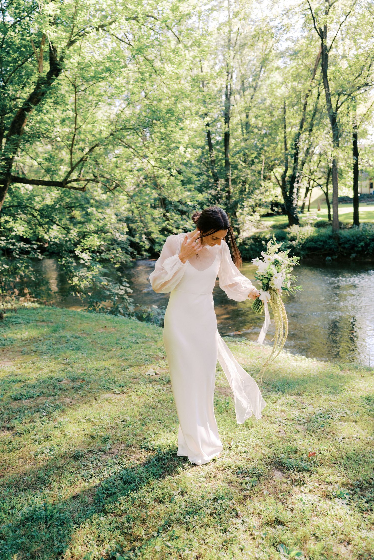 Flowing white wedding dress catches sunlight in a lush green garden setting.