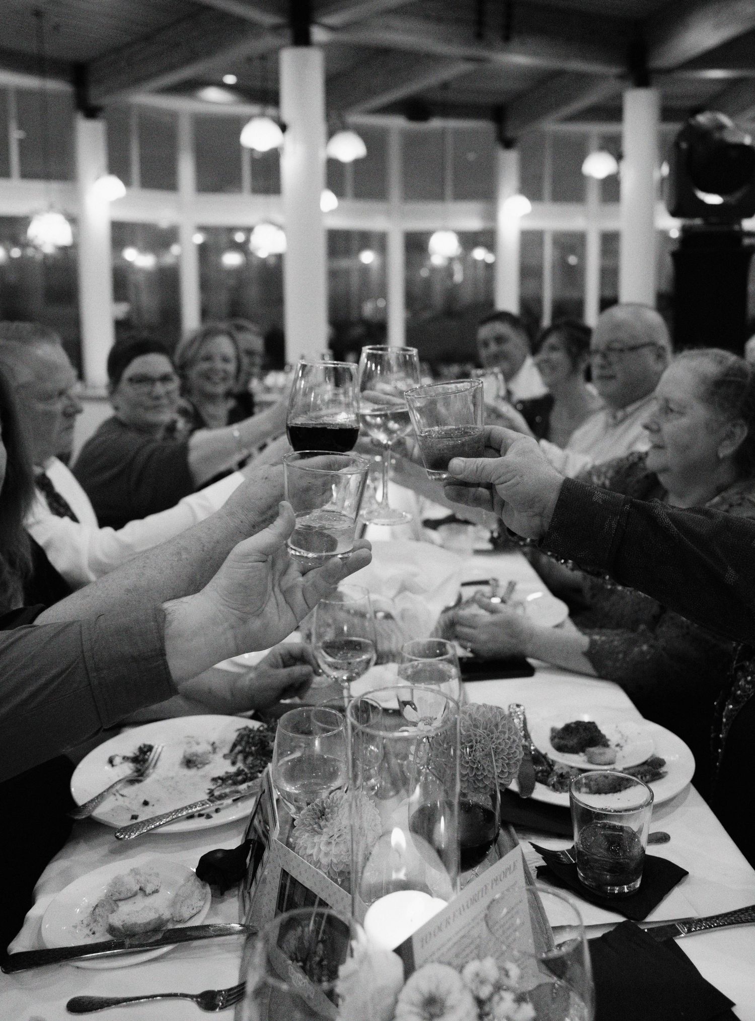 Black and white photo series of guests raising wine glasses in a toast during a wedding reception dinner.