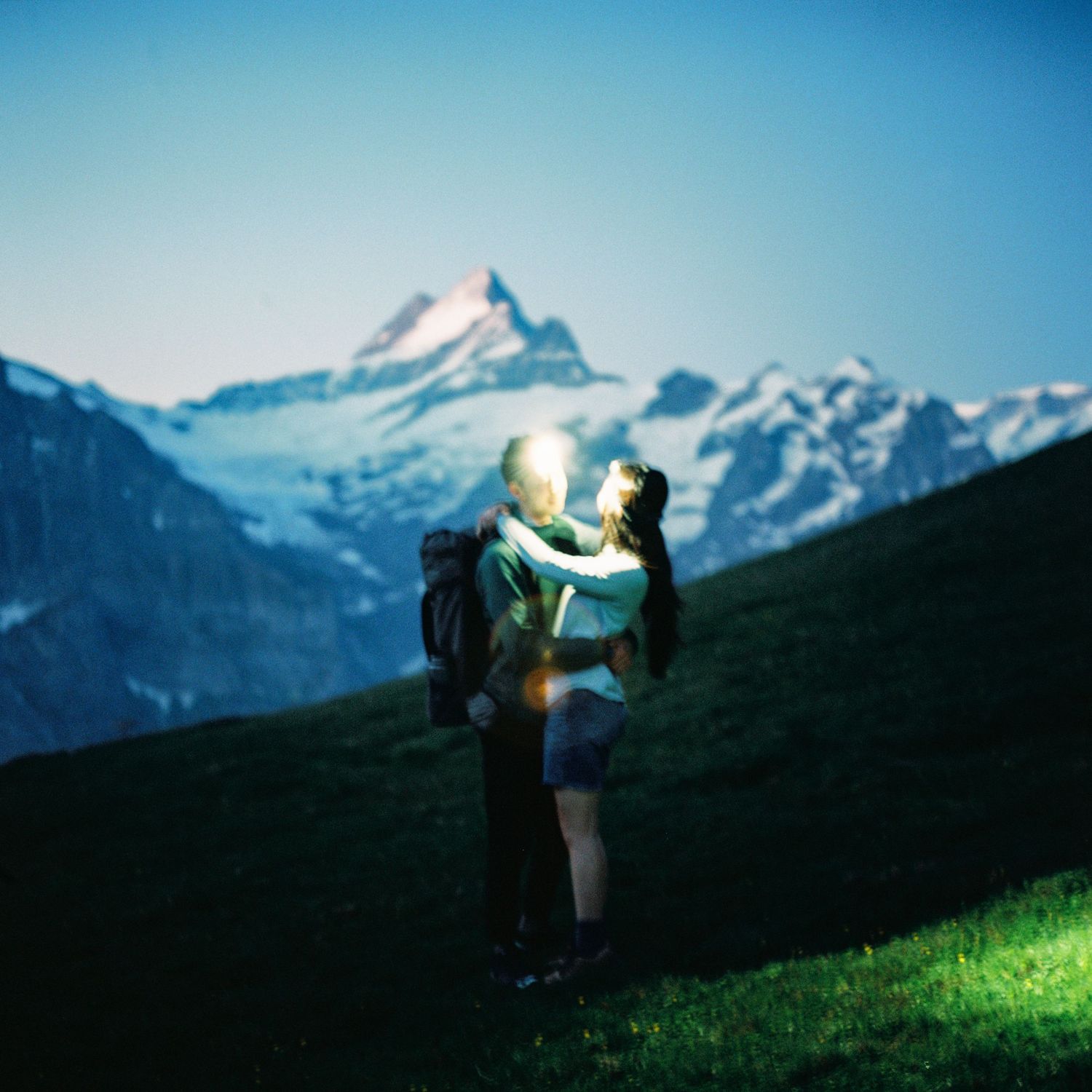 A couple embraces against a stunning backdrop of snow-capped mountain peaks in the Alps during a sunny day.