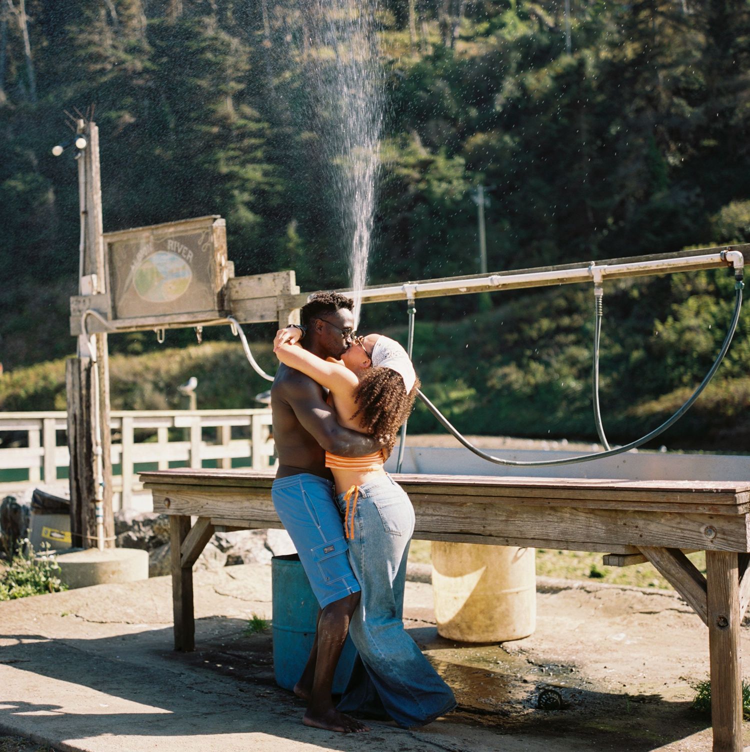 Couple sharing a romantic moment on a wooden bench overlooking a scenic mountain landscape on a sunny day.