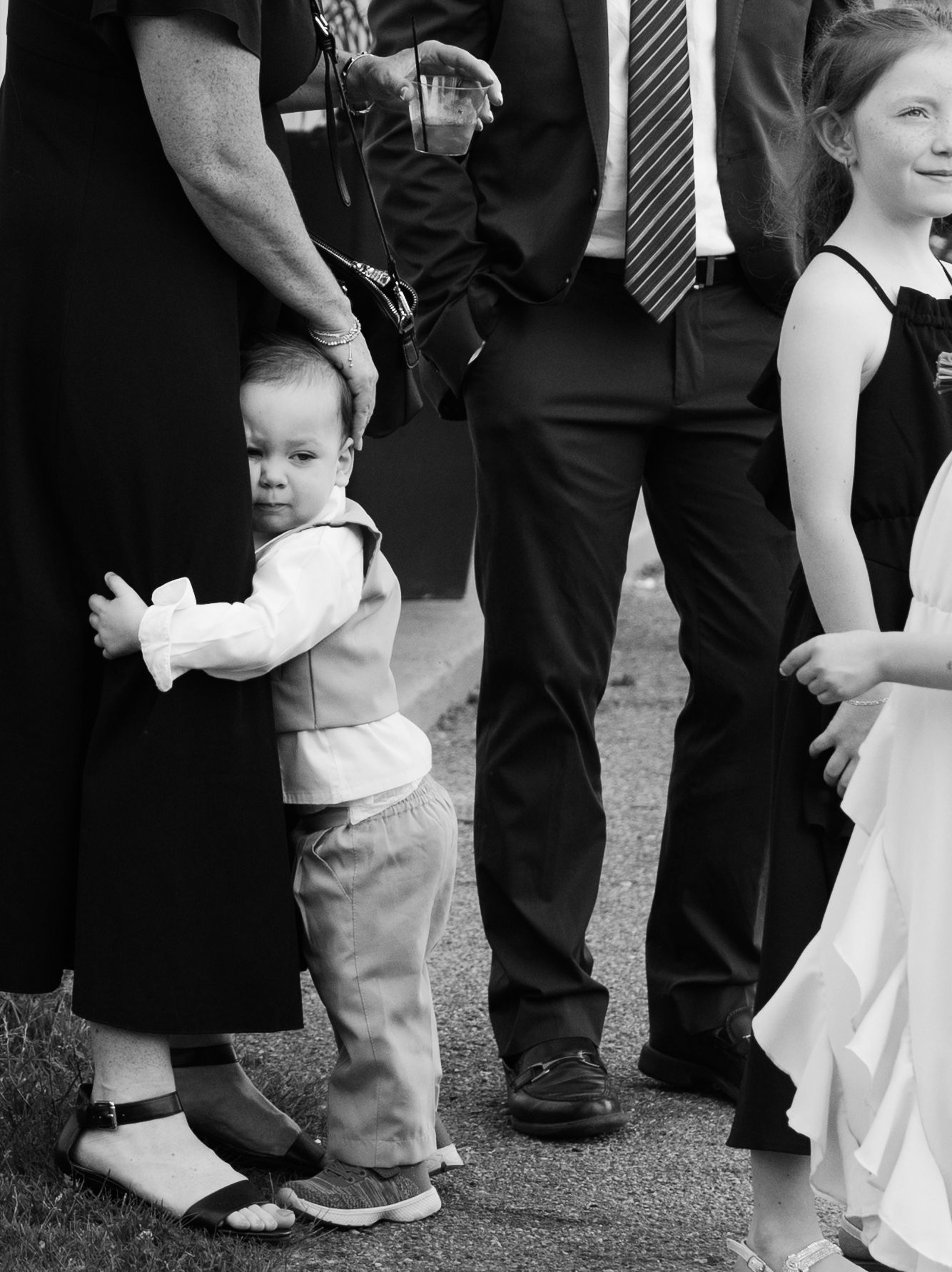 Black and white photo series showing children's feet and legs standing next to adults at a formal event.