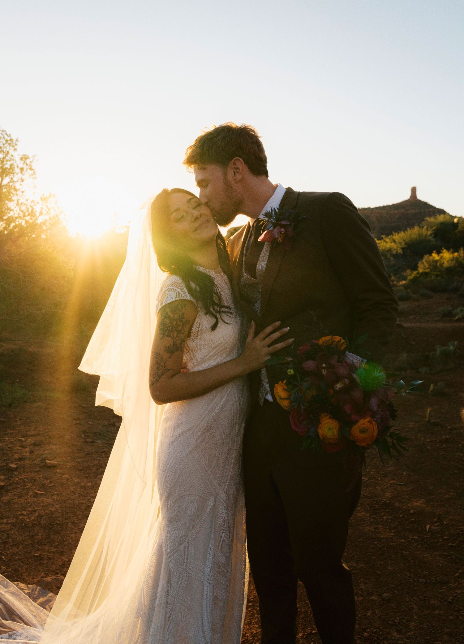 Romantic sunset wedding photo of newlyweds embracing outdoors with golden sunlight and long flowing veil.