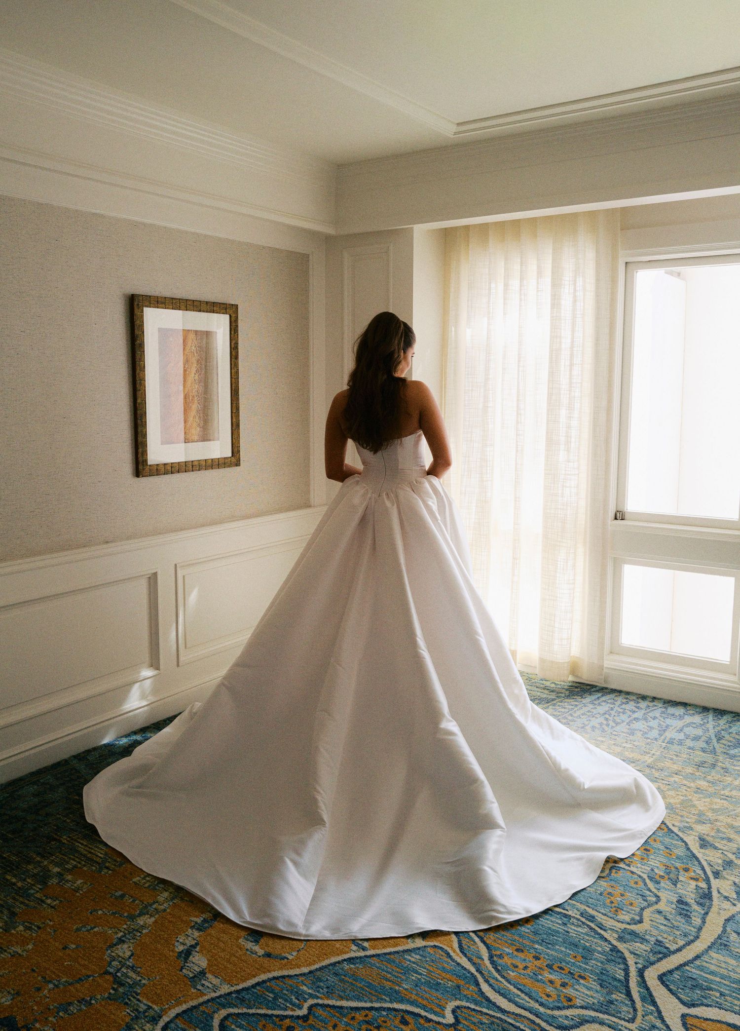 A flowing white wedding dress spins gracefully on a blue and cream patterned carpet in a sunlit room.