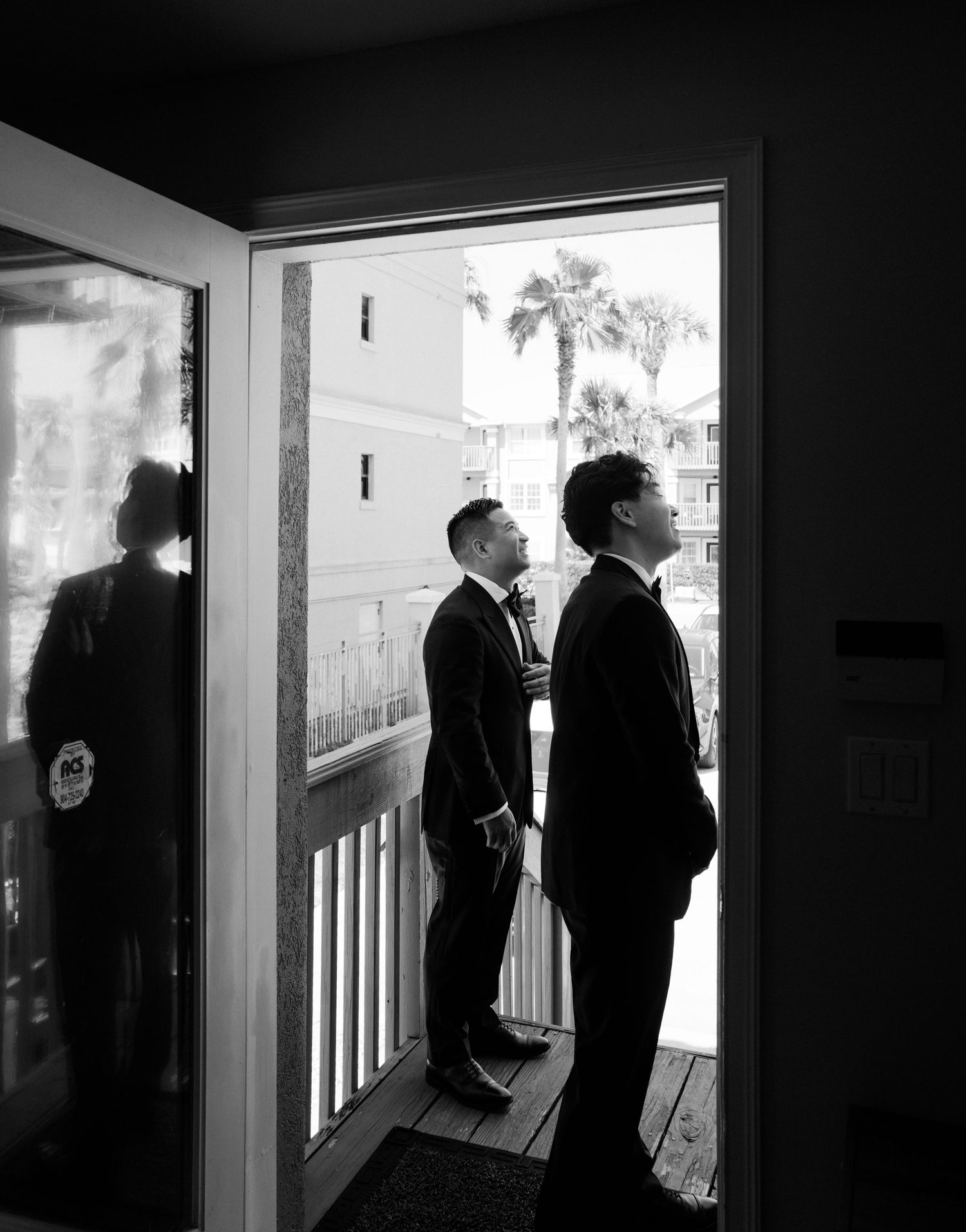 Black and white silhouettes of figures standing by a window during an intimate wedding moment.