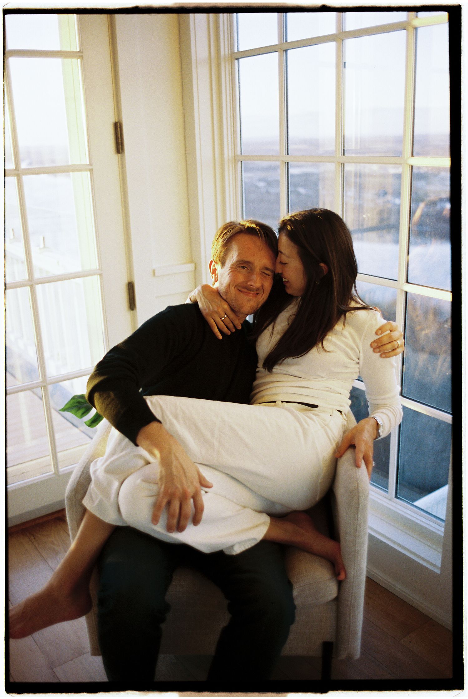 A couple shares intimate moments together while relaxing by a bright window in a casual indoor setting.