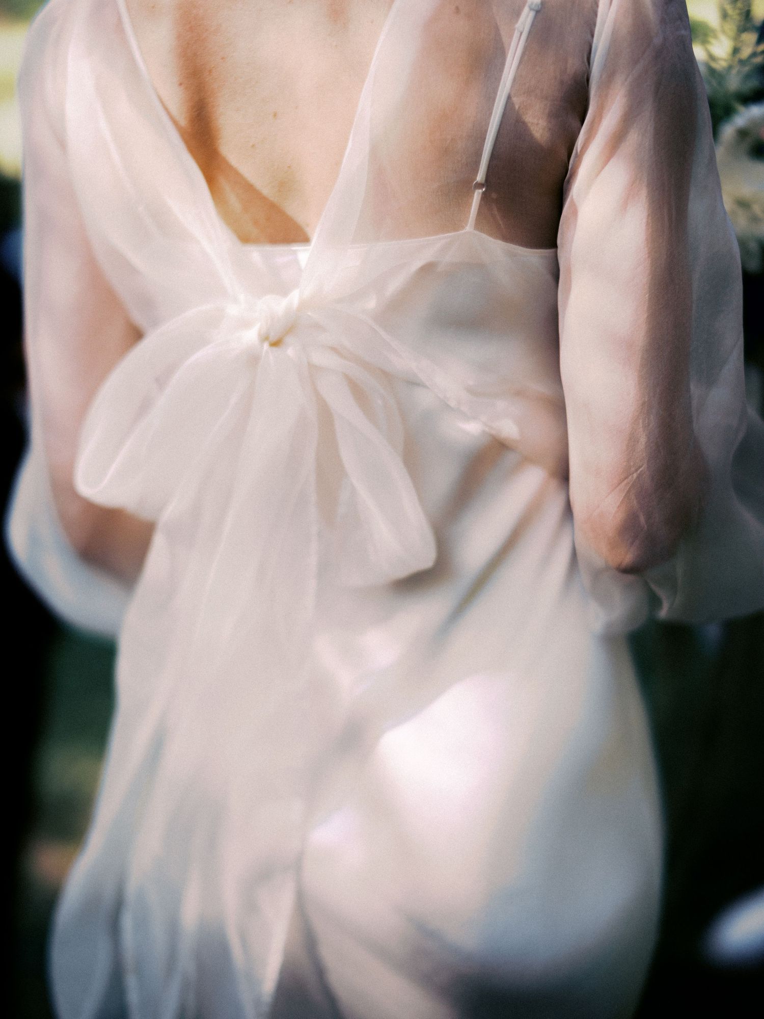 Close-up detail of white wedding dress bow and sheer fabric in soft natural light.