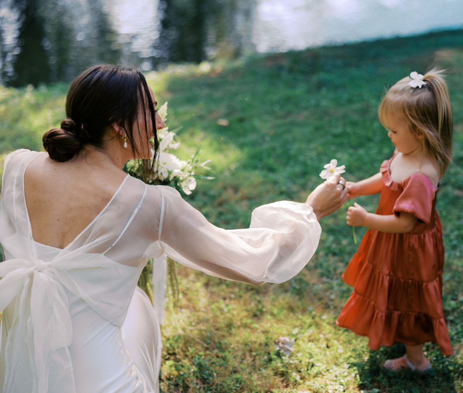 People in flowing dresses dance and twirl in a sunlit outdoor setting.