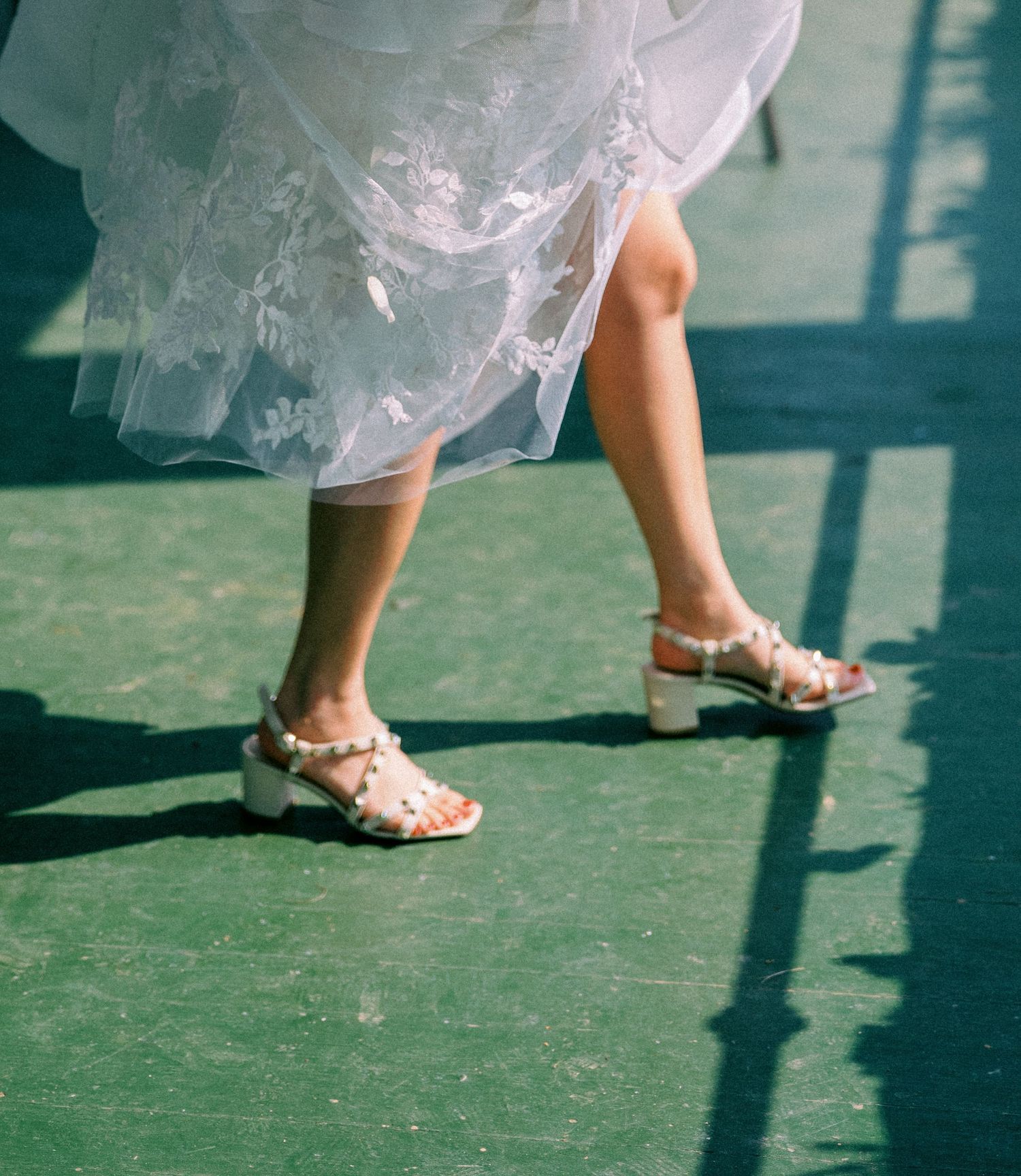 A series of wedding photos focusing on elegant white shoes and dress hem against a green lawn.
