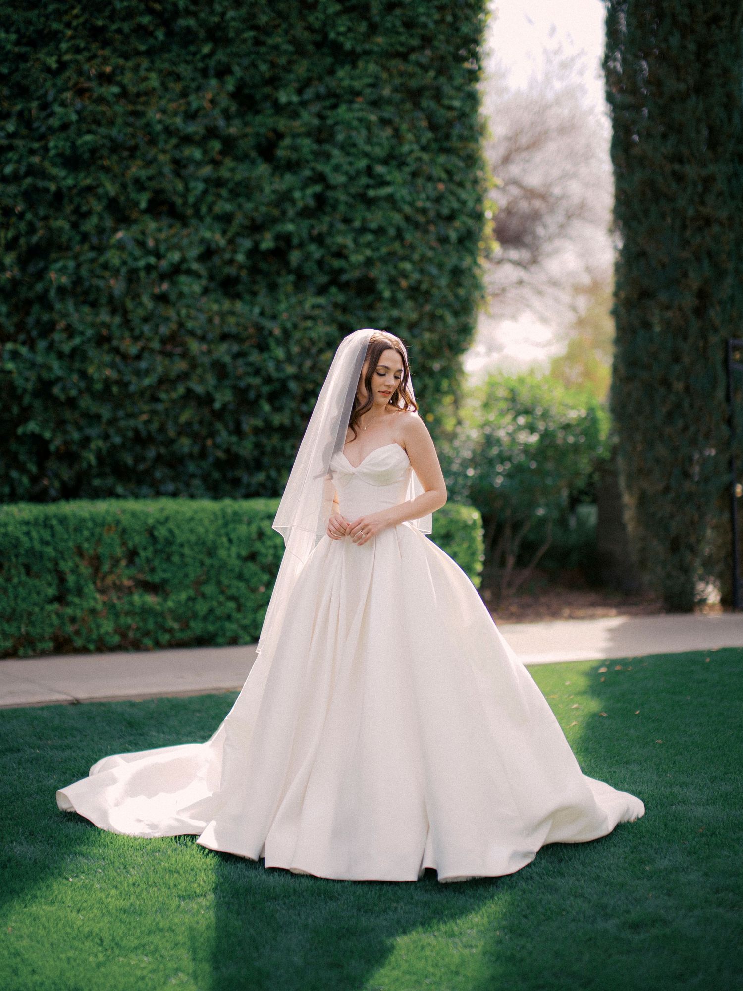 A bride in a flowing white ballgown twirls gracefully in a garden setting with lush greenery in the background.