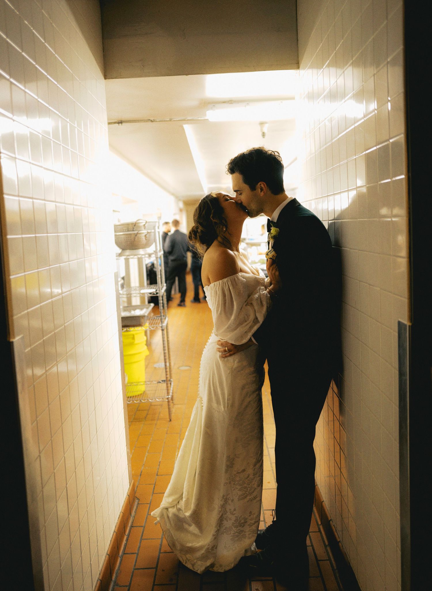 A couple walks through a brightly lit white corridor in formal attire.