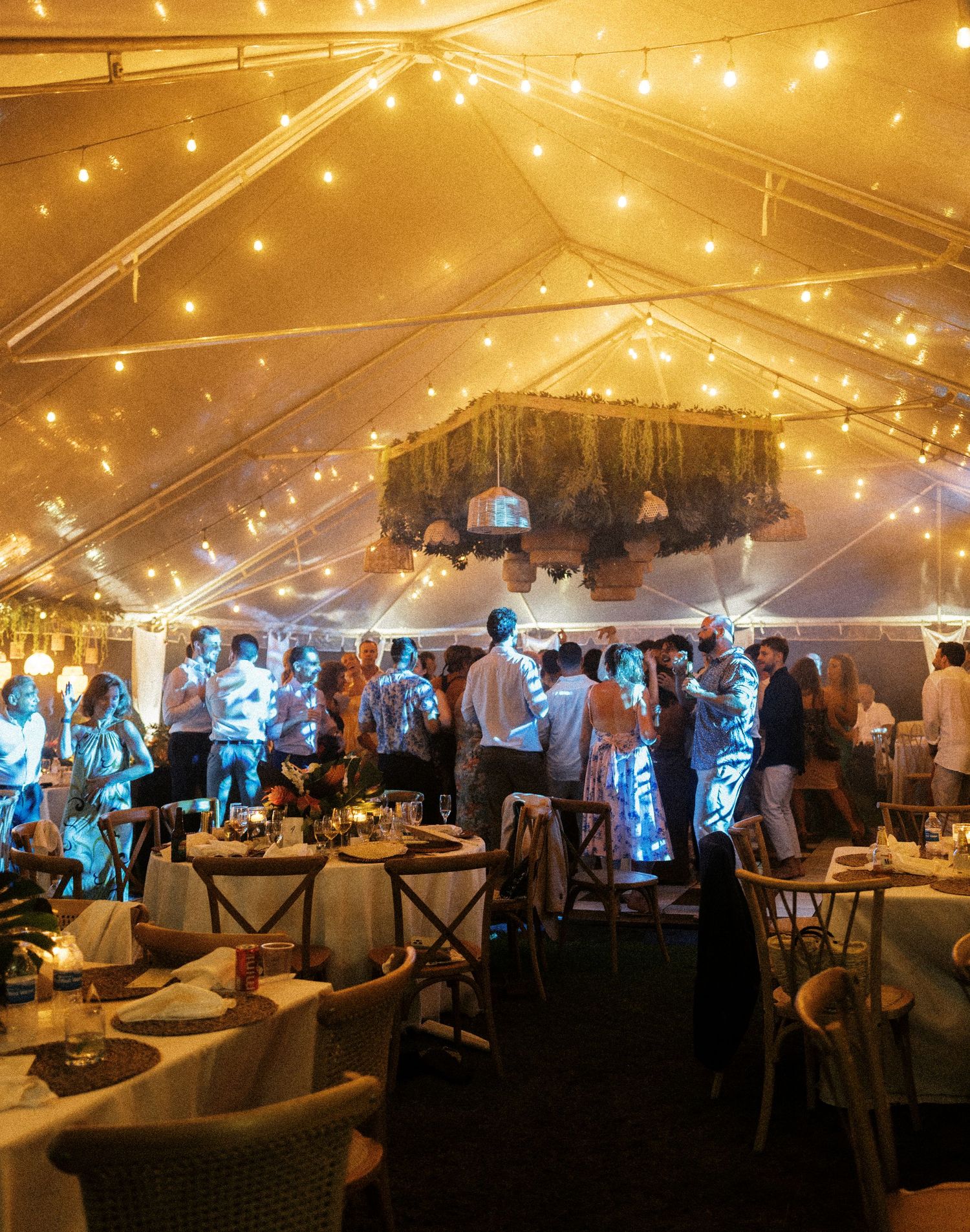 Panoramic view of an elegant wedding reception under a tent with twinkling string lights creating a warm, romantic atmosphere.