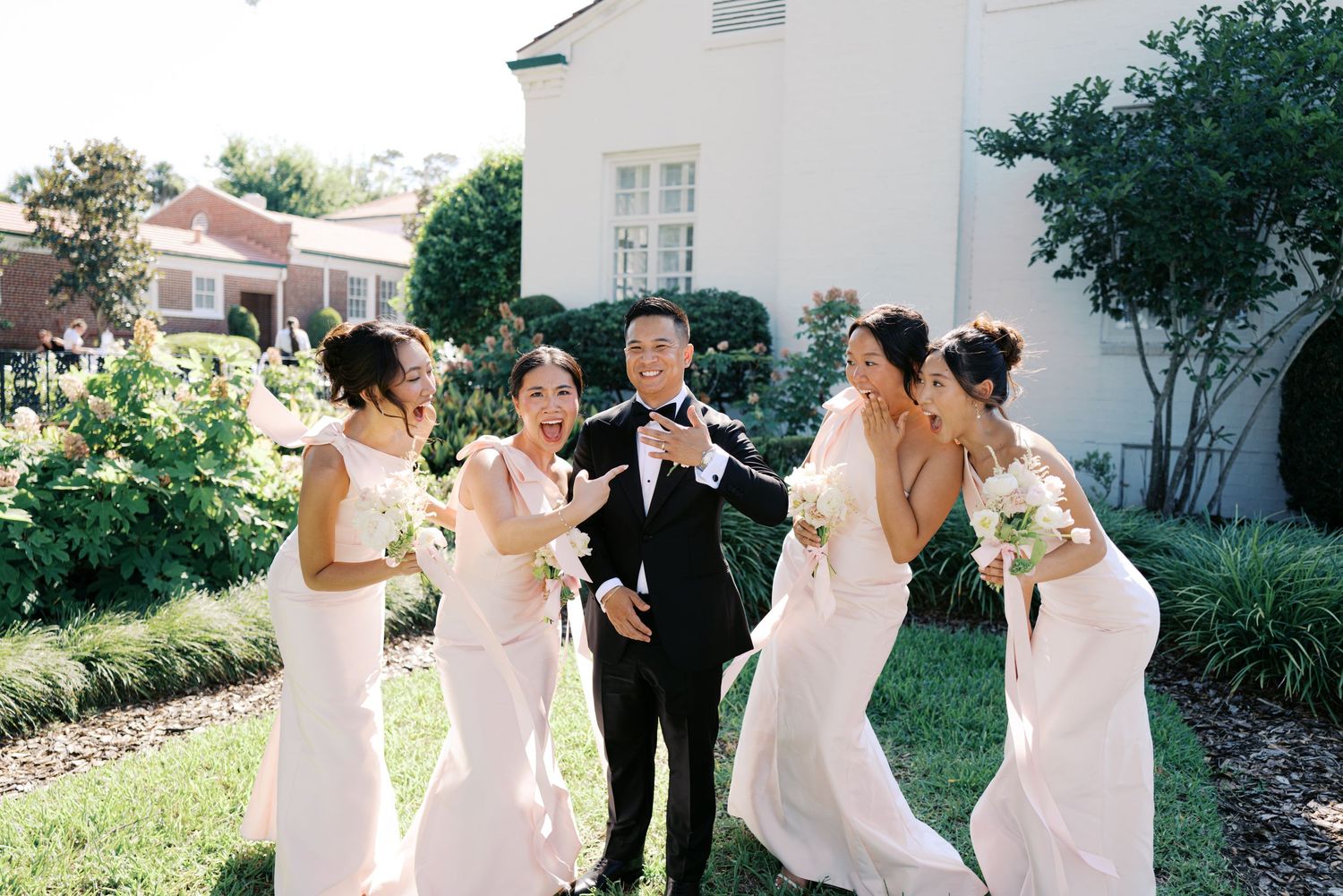 Wedding party in black and pink attire takes celebratory drinks together outdoors.