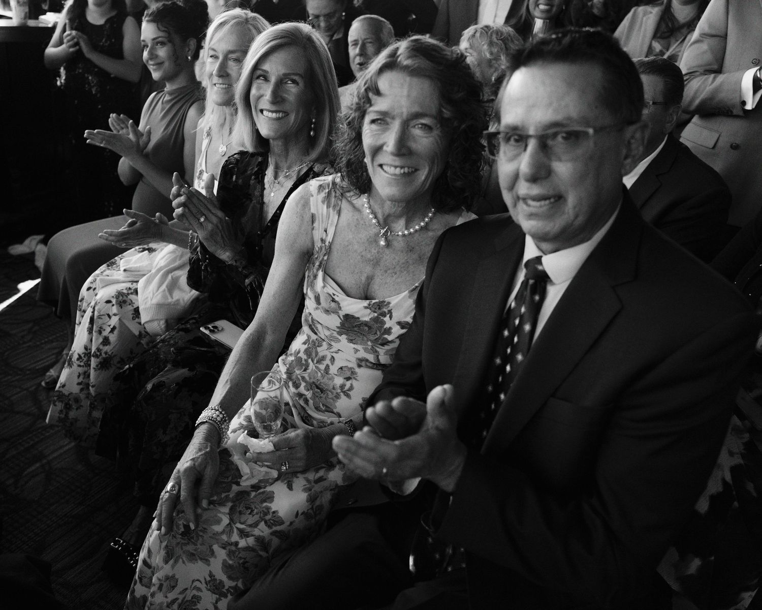 Black and white photo of audience members sitting in theater seats, with a couple in formal attire smiling at the camera.