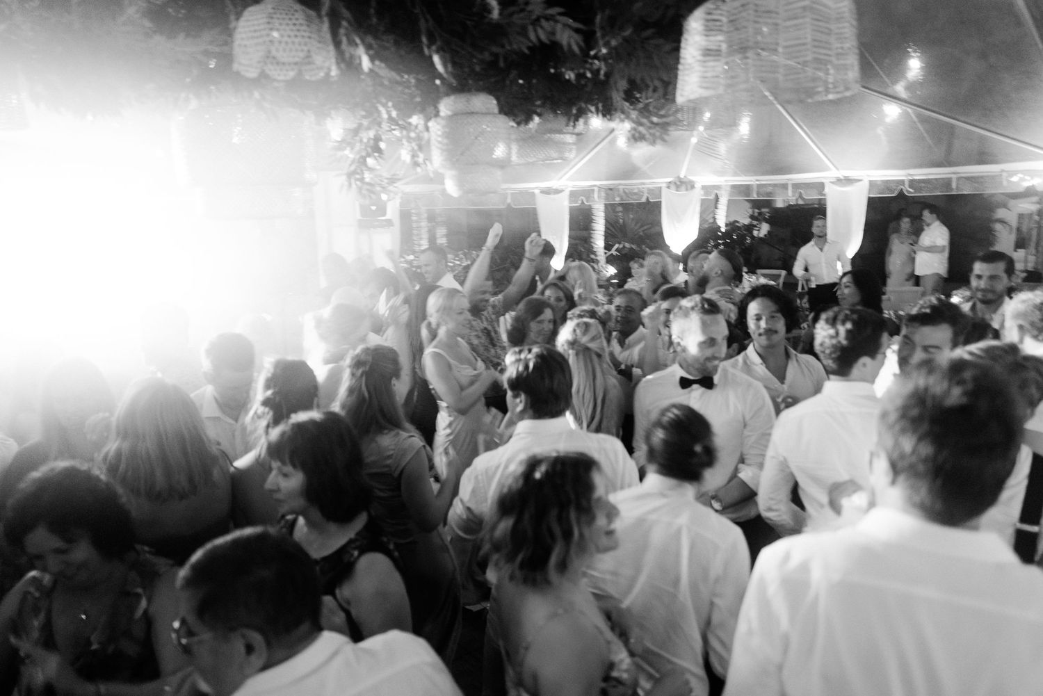 A crowded dance floor filled with people enjoying a lively party under glowing string lights and disco lighting.