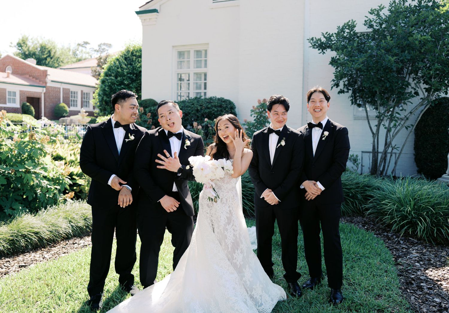 Wedding party in formal attire posing together outdoors on a sunny day.