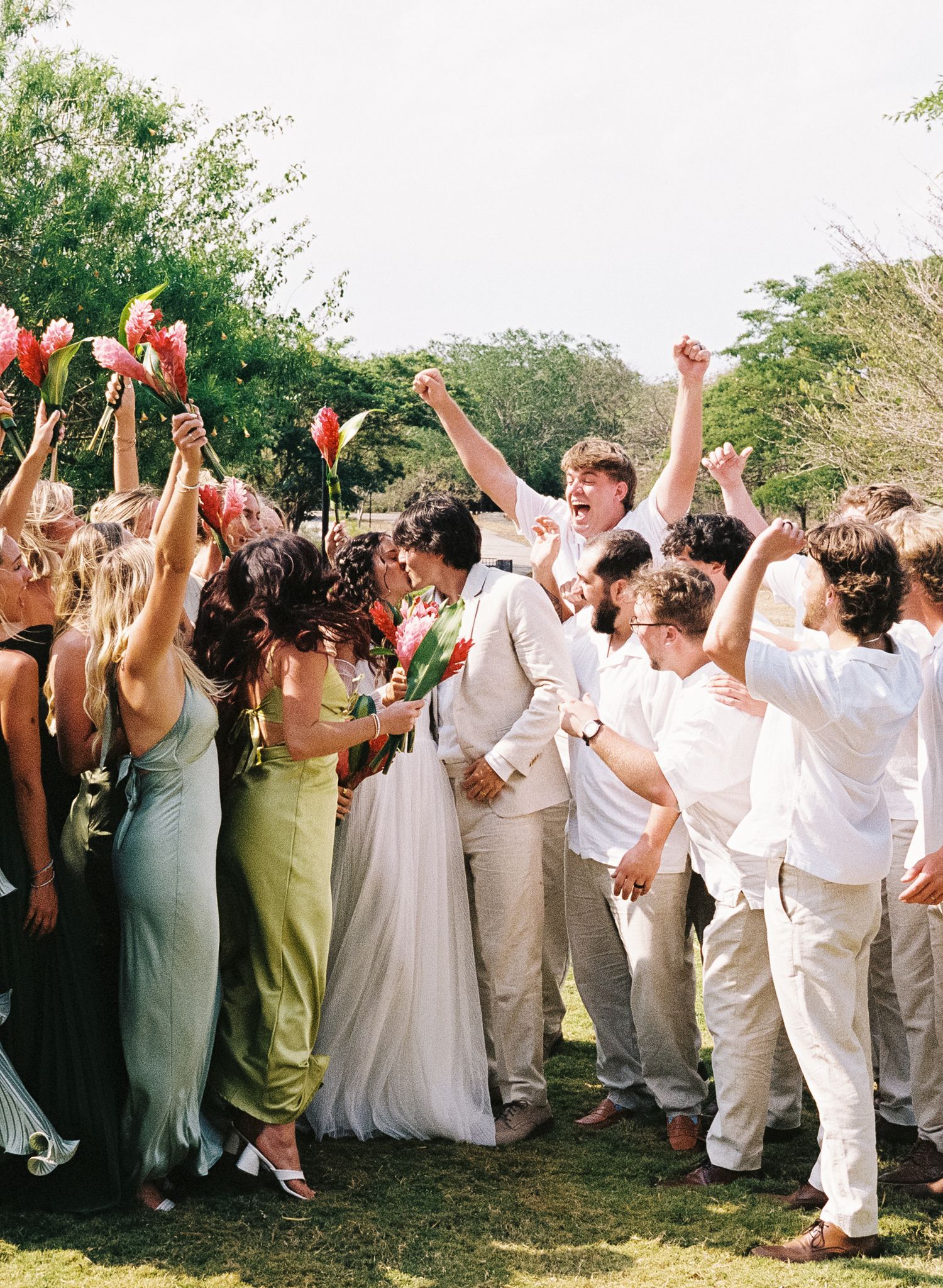 Wedding guests celebrate joyfully in white attire with raised arms during an outdoor celebration.