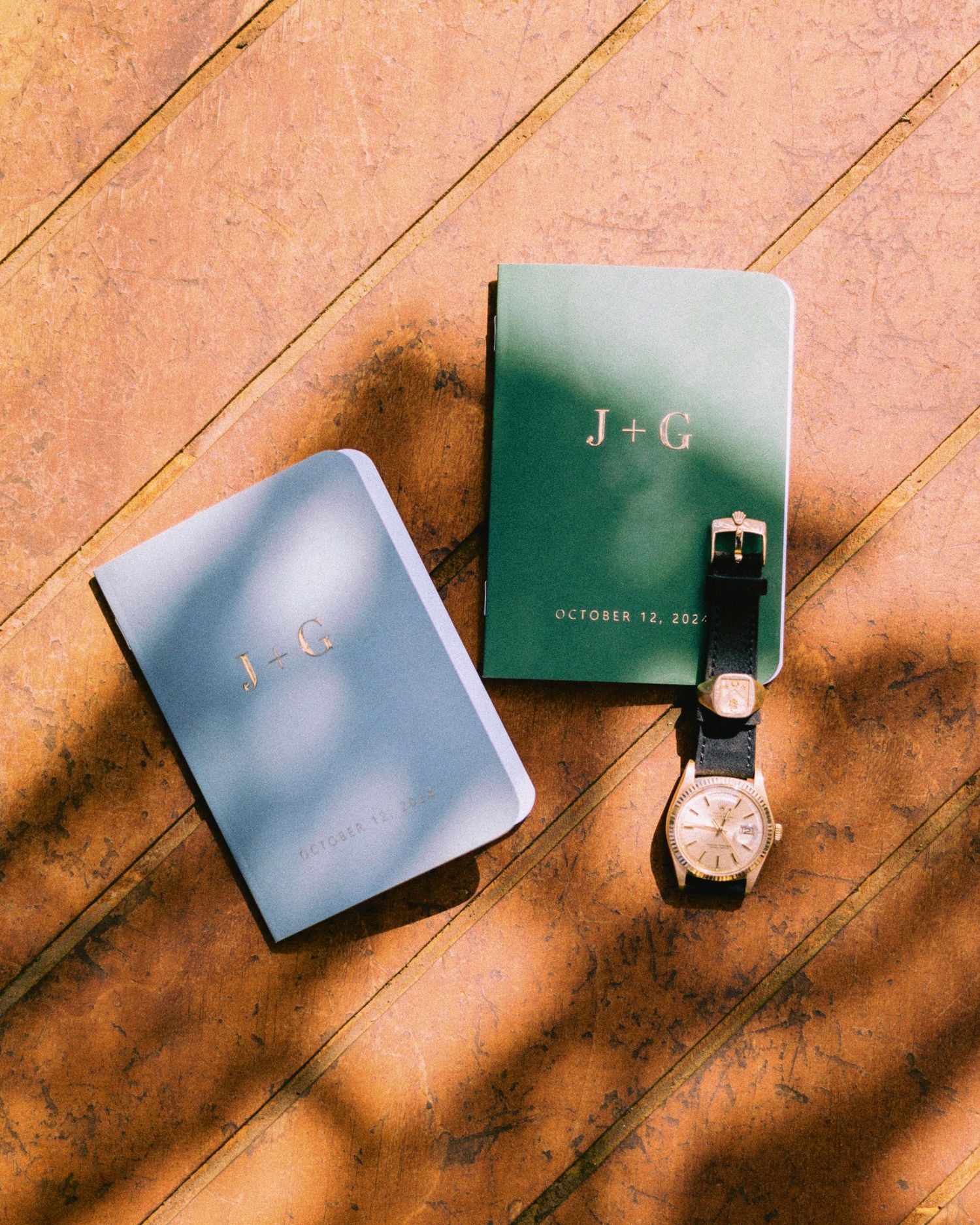 Elegant green and silver wedding invitation cards with a watch arranged on a wooden surface in warm lighting.
