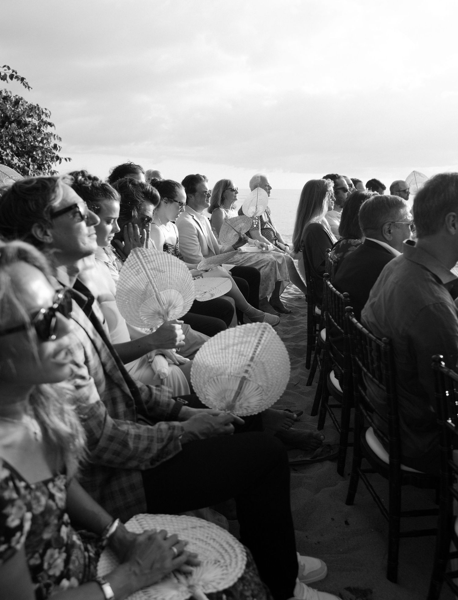 A black and white photograph shows a group of people seated in rows reading newspapers during a public gathering.