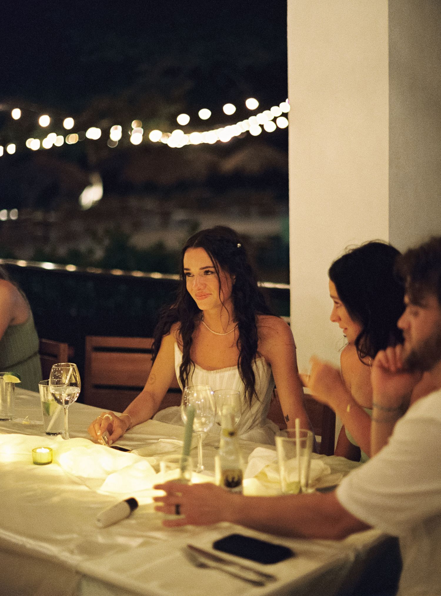 Evening dinner scene with string lights and glassware on a white tablecloth.