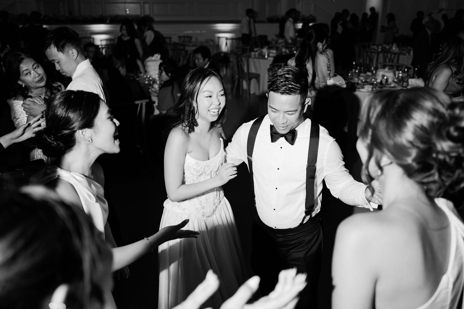 Black and white photo of wedding guests dancing energetically at a reception party.