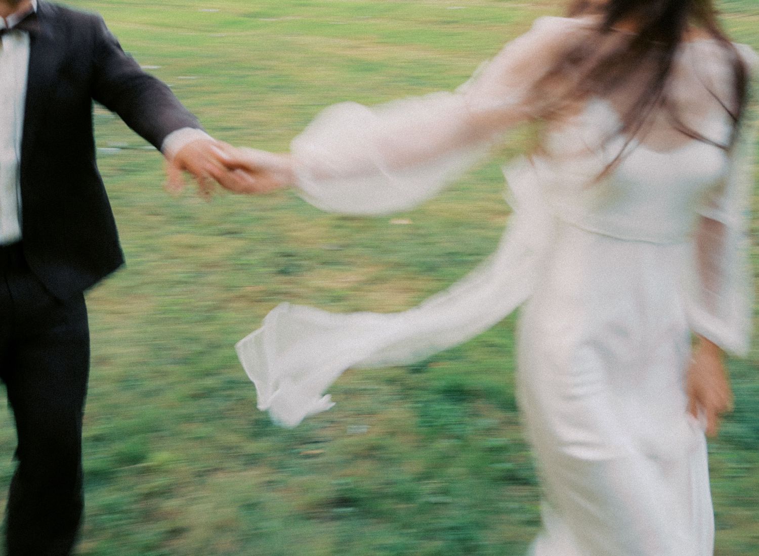 Motion-blurred couple dancing on grass with flowing white dress creating ethereal movement.