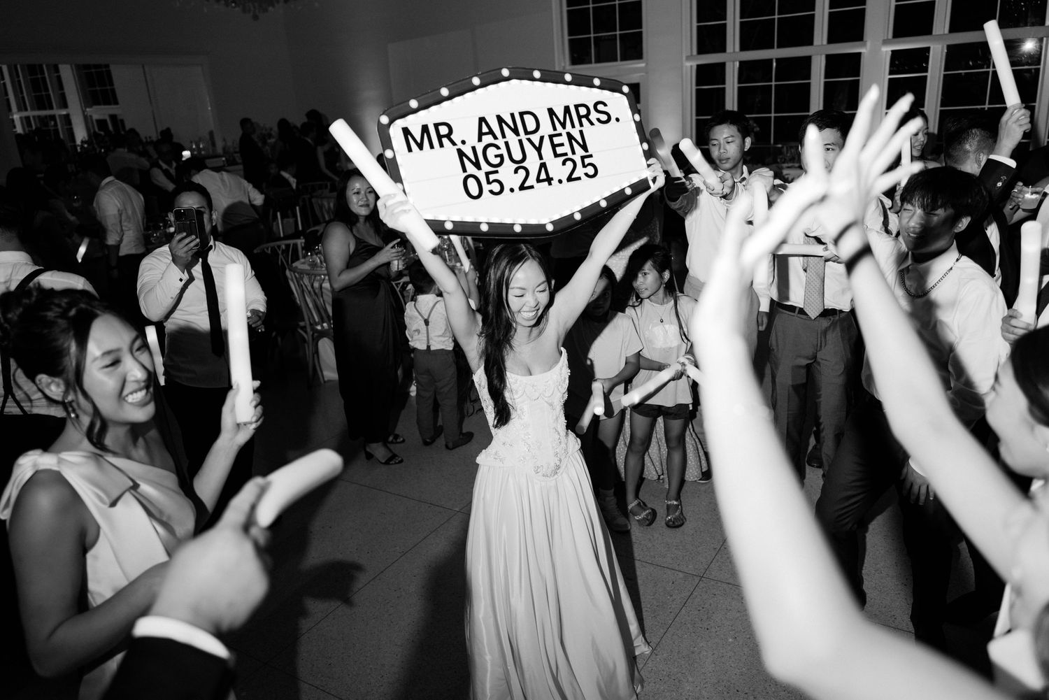 Wedding reception party crowd dancing and celebrating with Mr and Mrs sign held high in black and white.