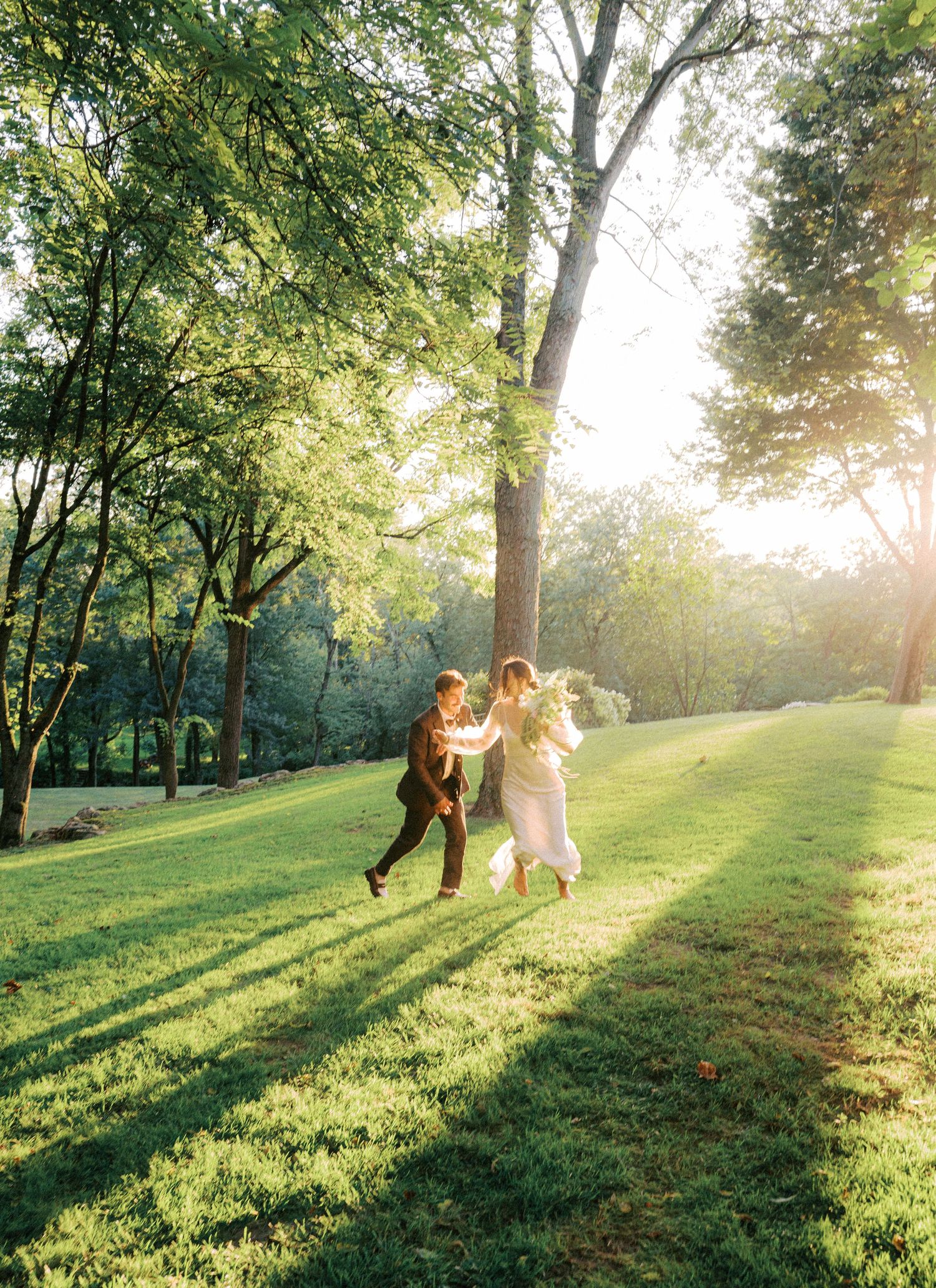 Sunlit outdoor wedding ceremony setting with golden light streaming through trees on a grassy hillside.
