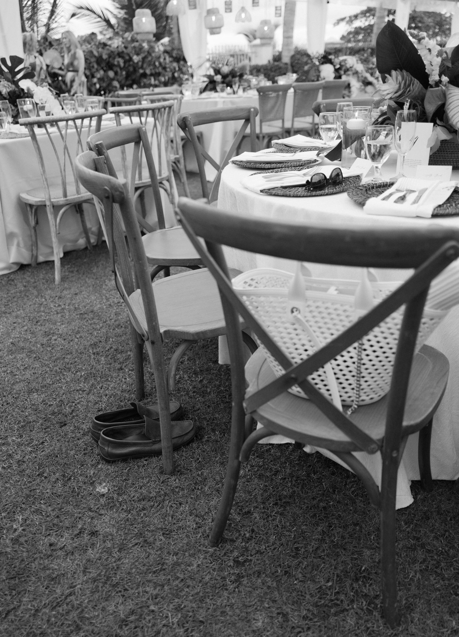Black and white image showing multiple tables set up outdoors with checkered tablecloths and chairs.