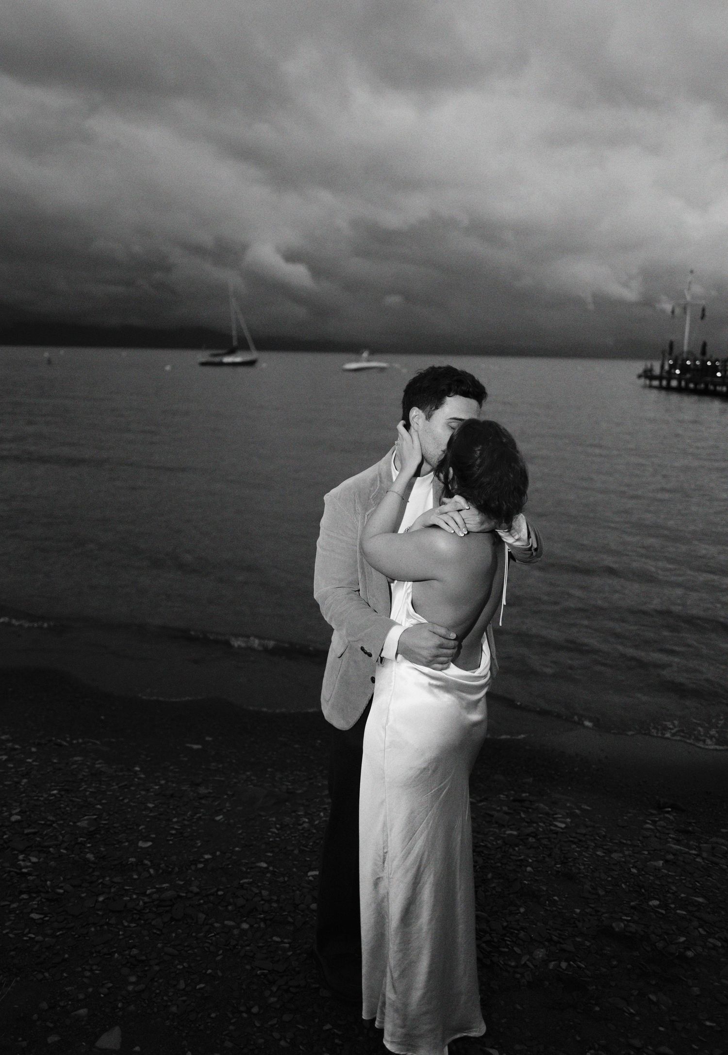 A romantic black and white beach wedding photo series showing an intimate embrace against a stormy ocean backdrop.