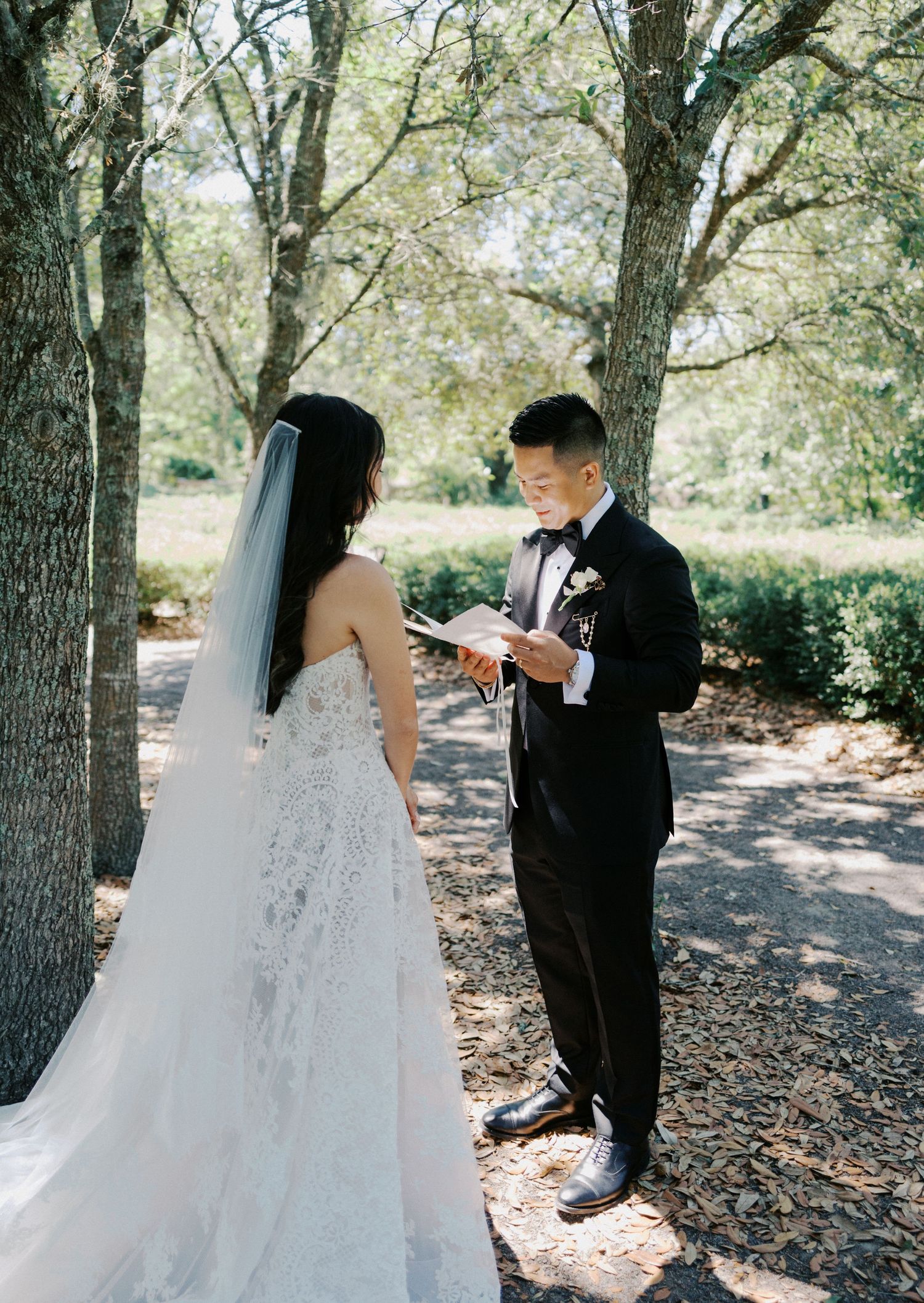A couple shares a private first look moment under oak trees in a wooded outdoor setting.