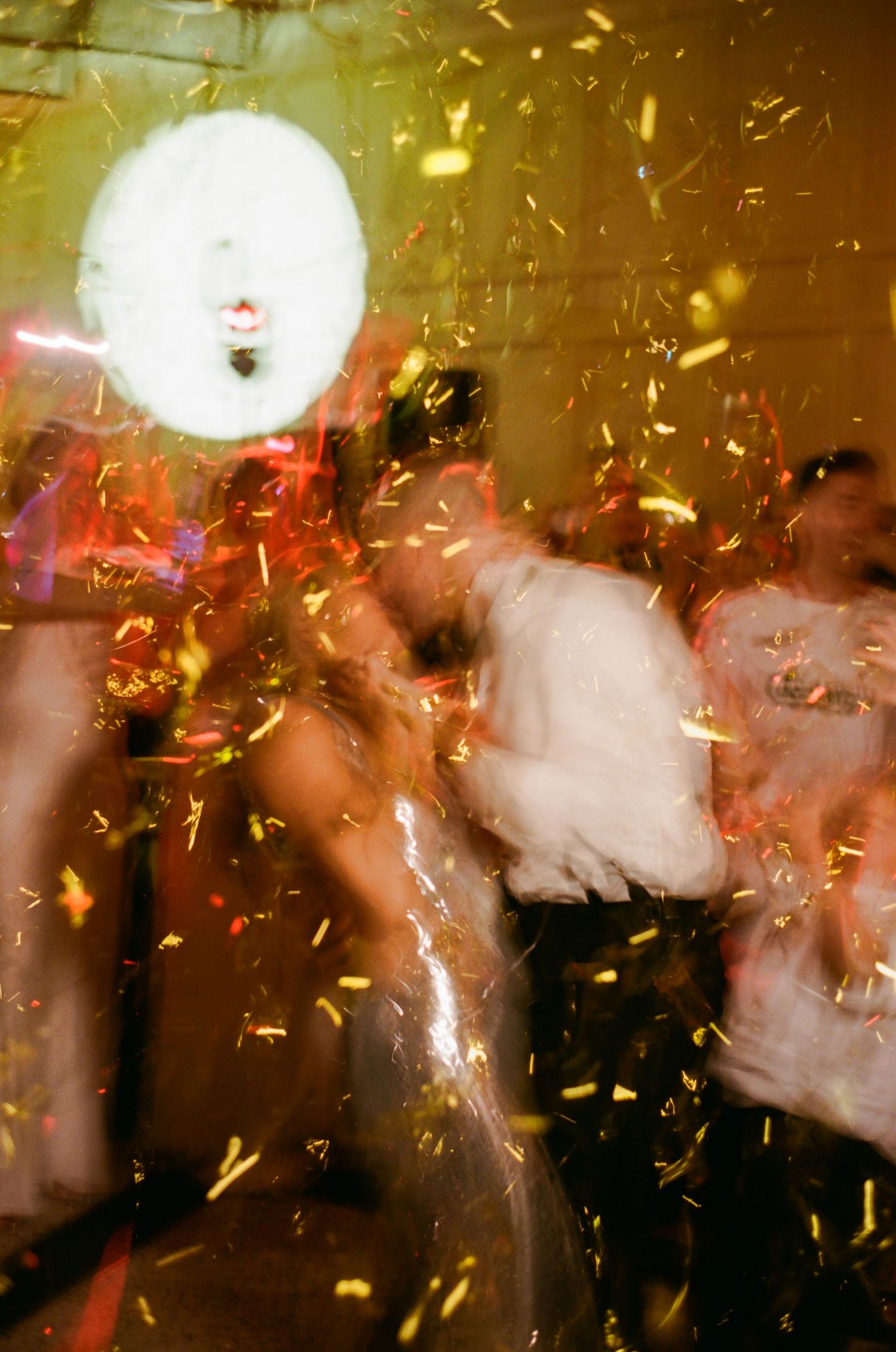 Blurred motion photo of a nightclub party scene with golden confetti falling through red and amber lighting.