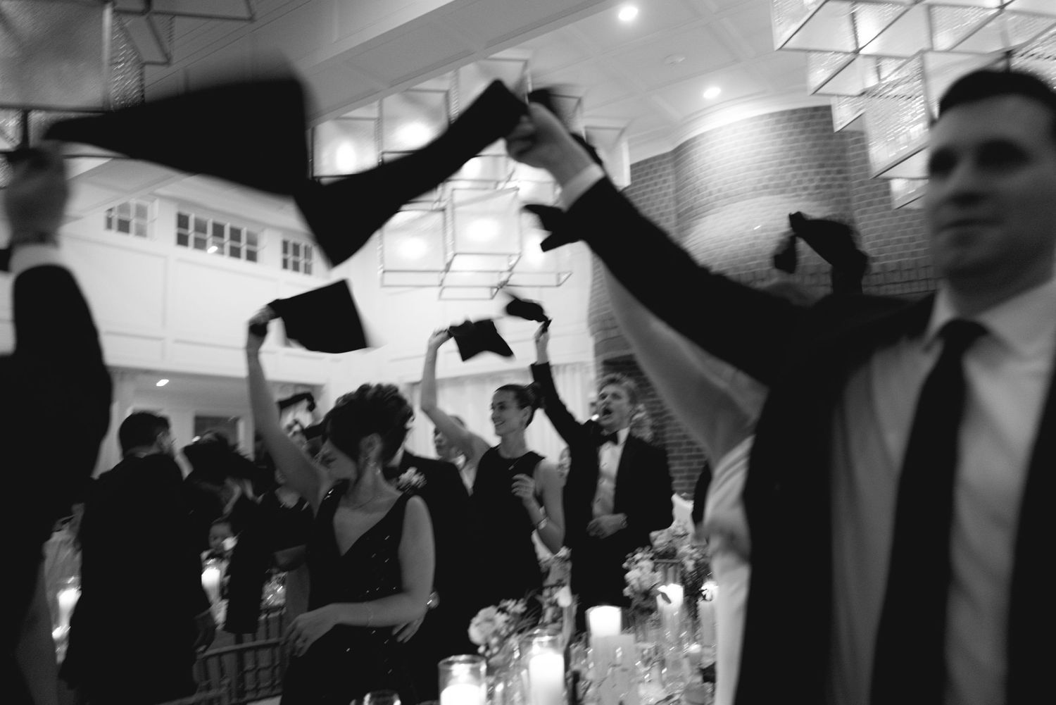 Black and white photo of a celebratory reception or party with people raising their arms in joyful dance moves.