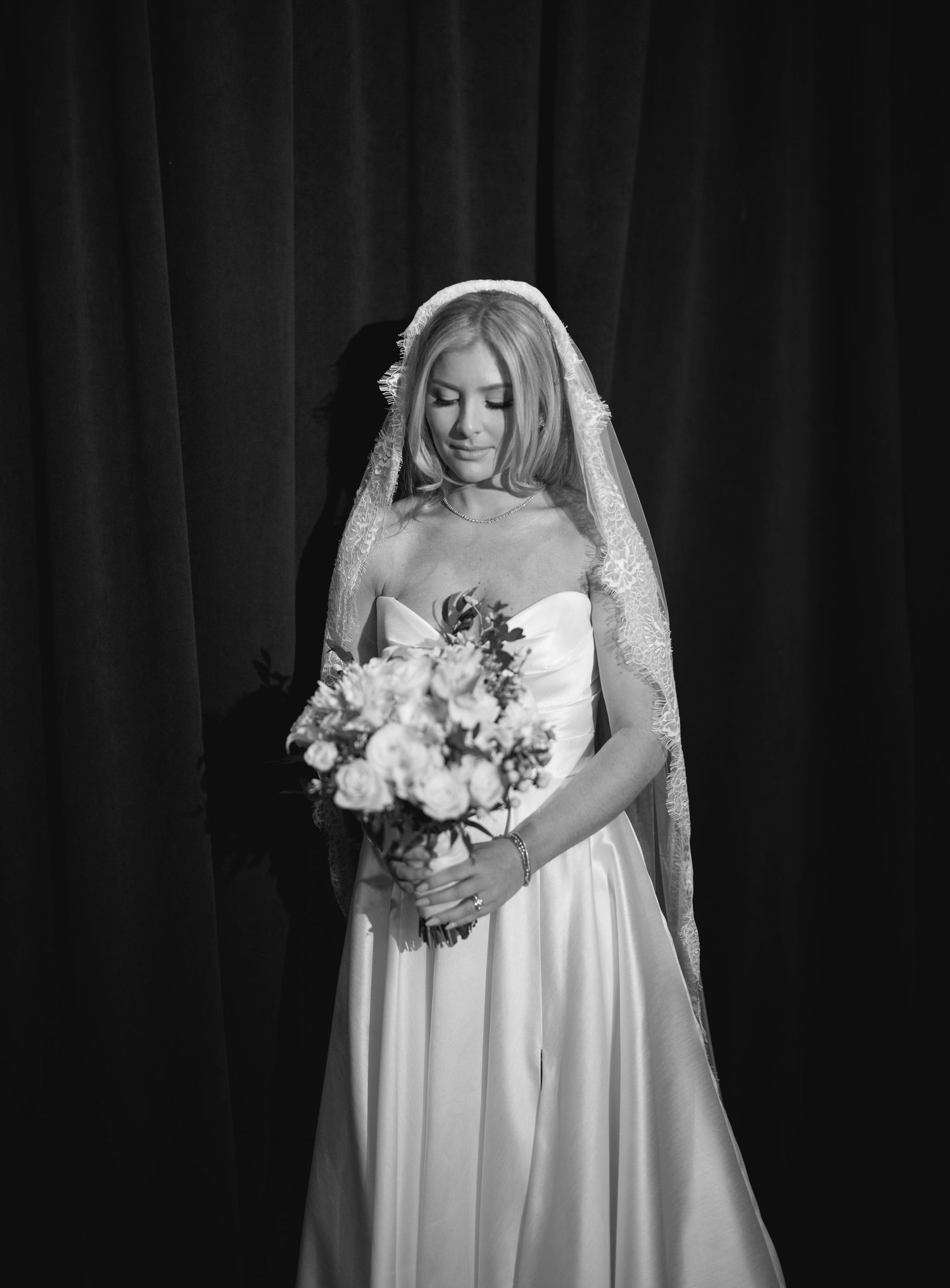 Black and white portrait of a bride in a flowing white gown holding a romantic bouquet of flowers.
