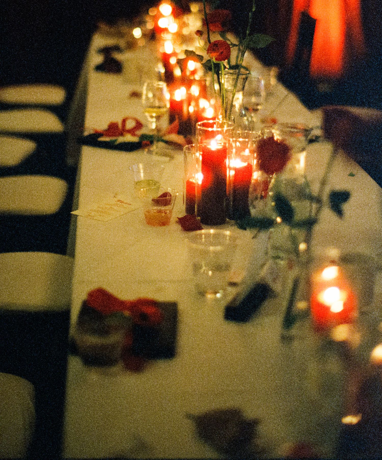 An elegant wedding reception table set with glowing red candles and glassware in romantic lighting.