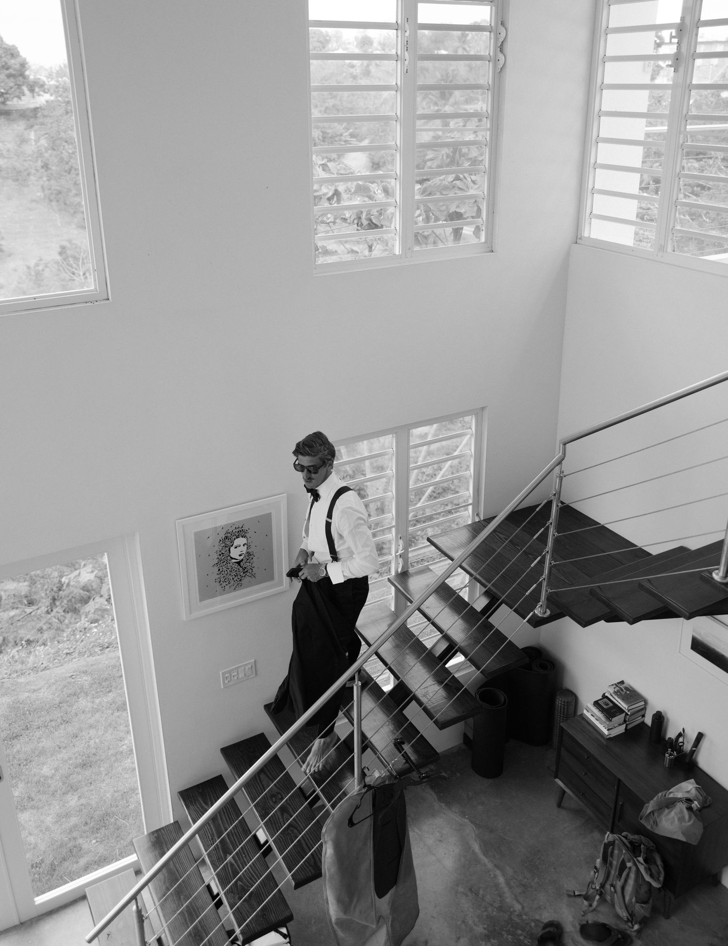 Black and white photo of someone in business attire standing on modern staircase with large windows and natural light.
