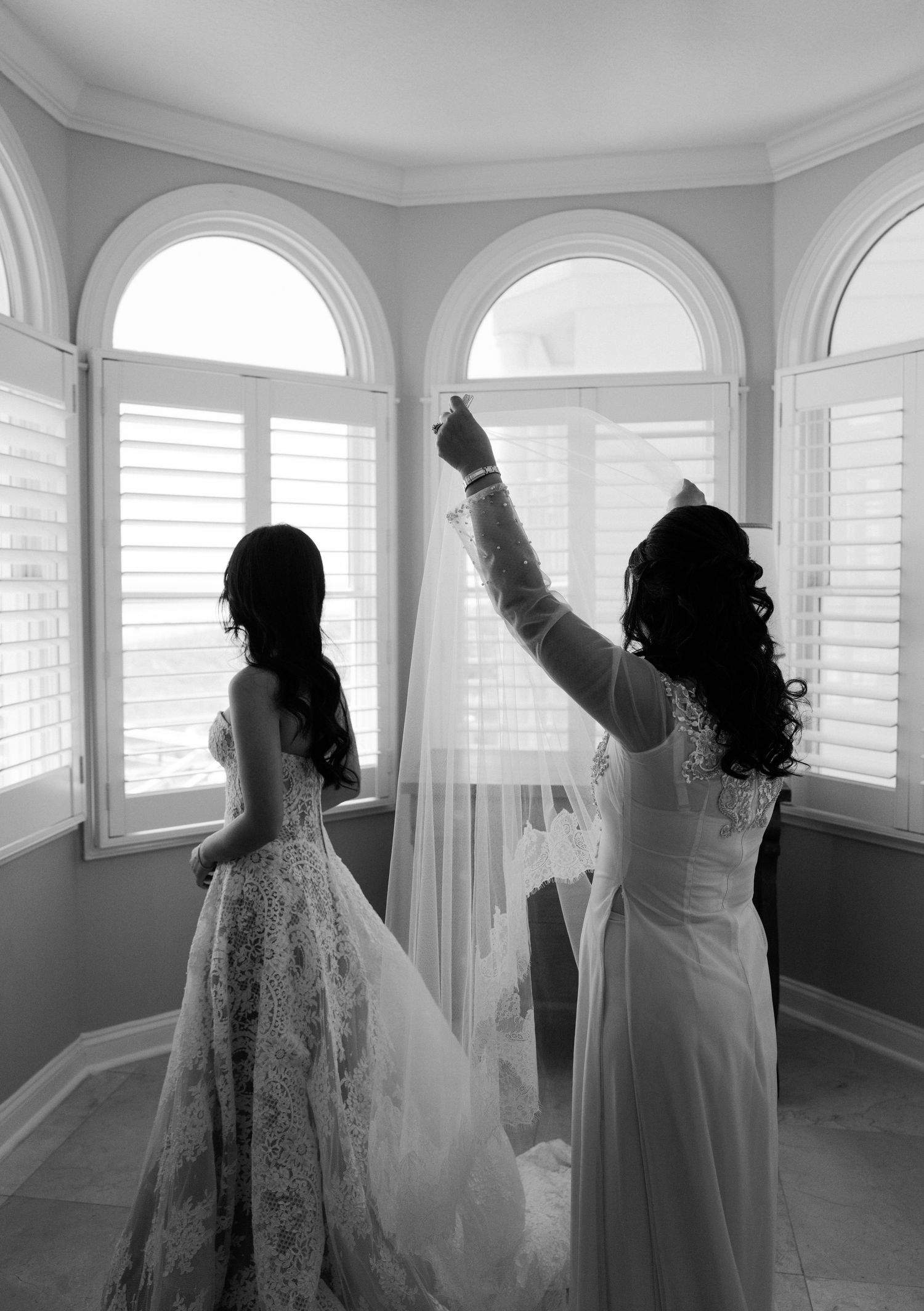 Silhouettes of wedding party members dancing and celebrating in a bright white room with arched windows.
