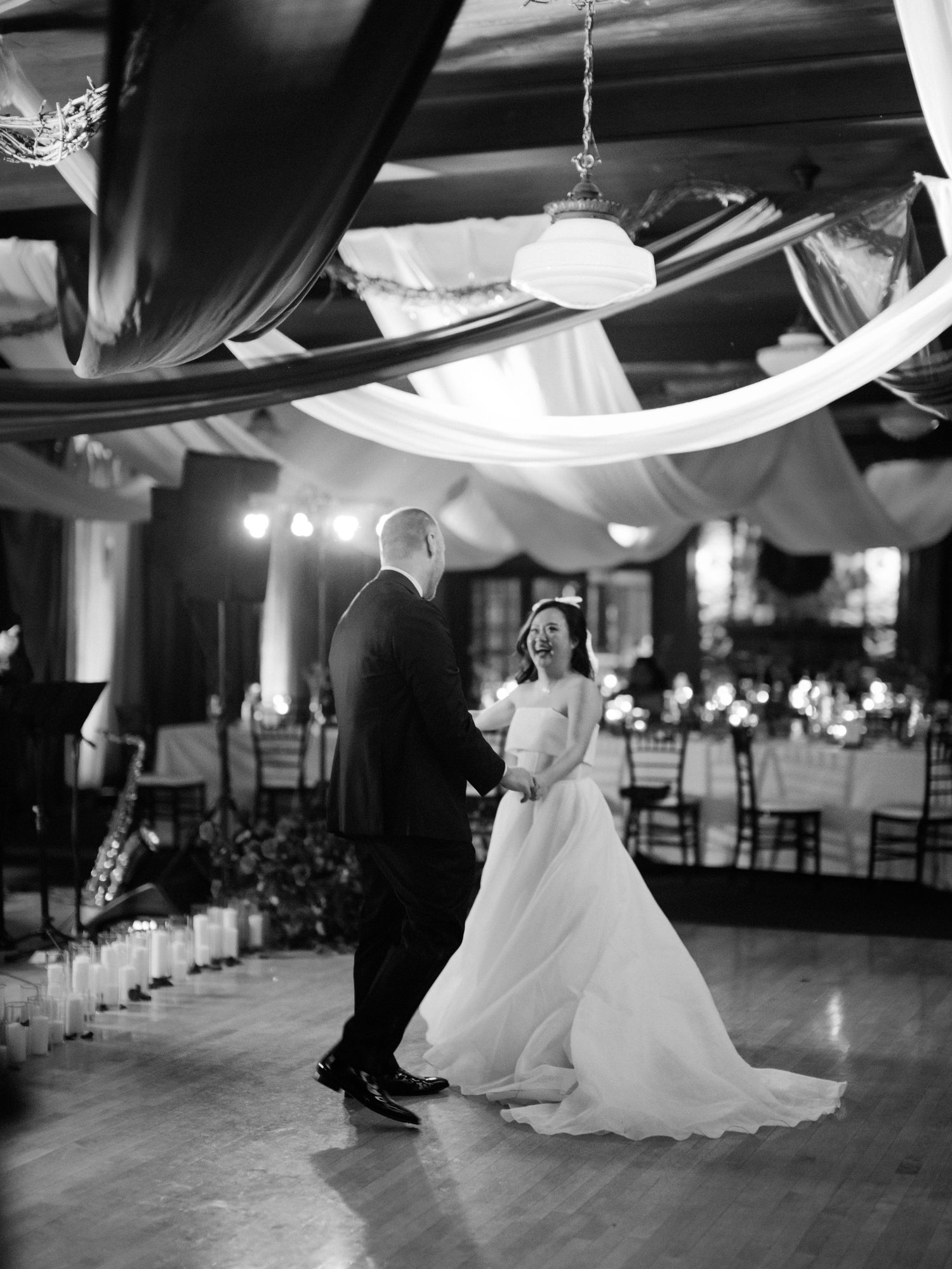 A couple shares their first dance under elegant draped fabric and lighting at their wedding reception.