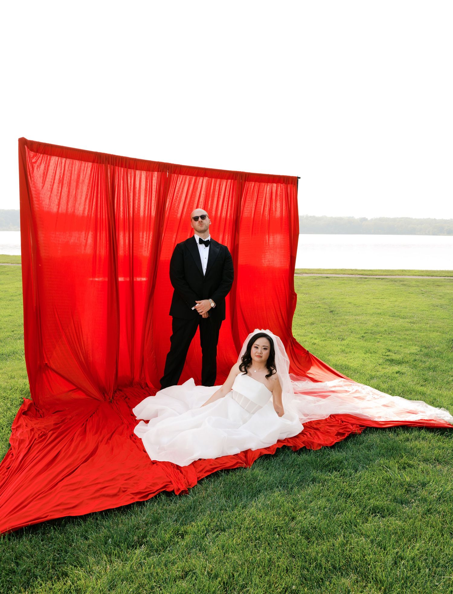 Creative wedding photos against dramatic red backdrop on grassy field.