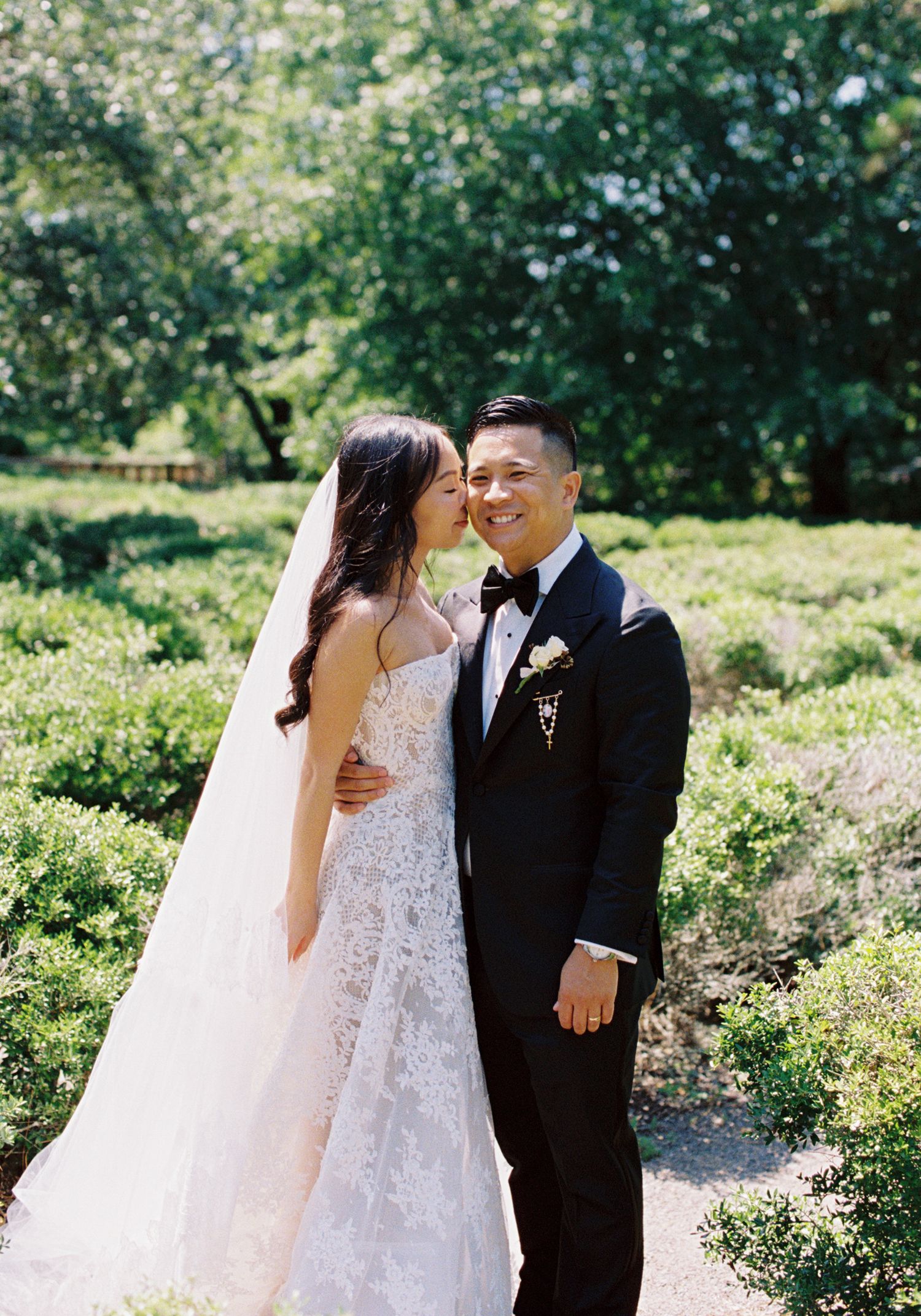 A couple shares tender moments in a lush garden setting during their wedding photoshoot on a sunny day.