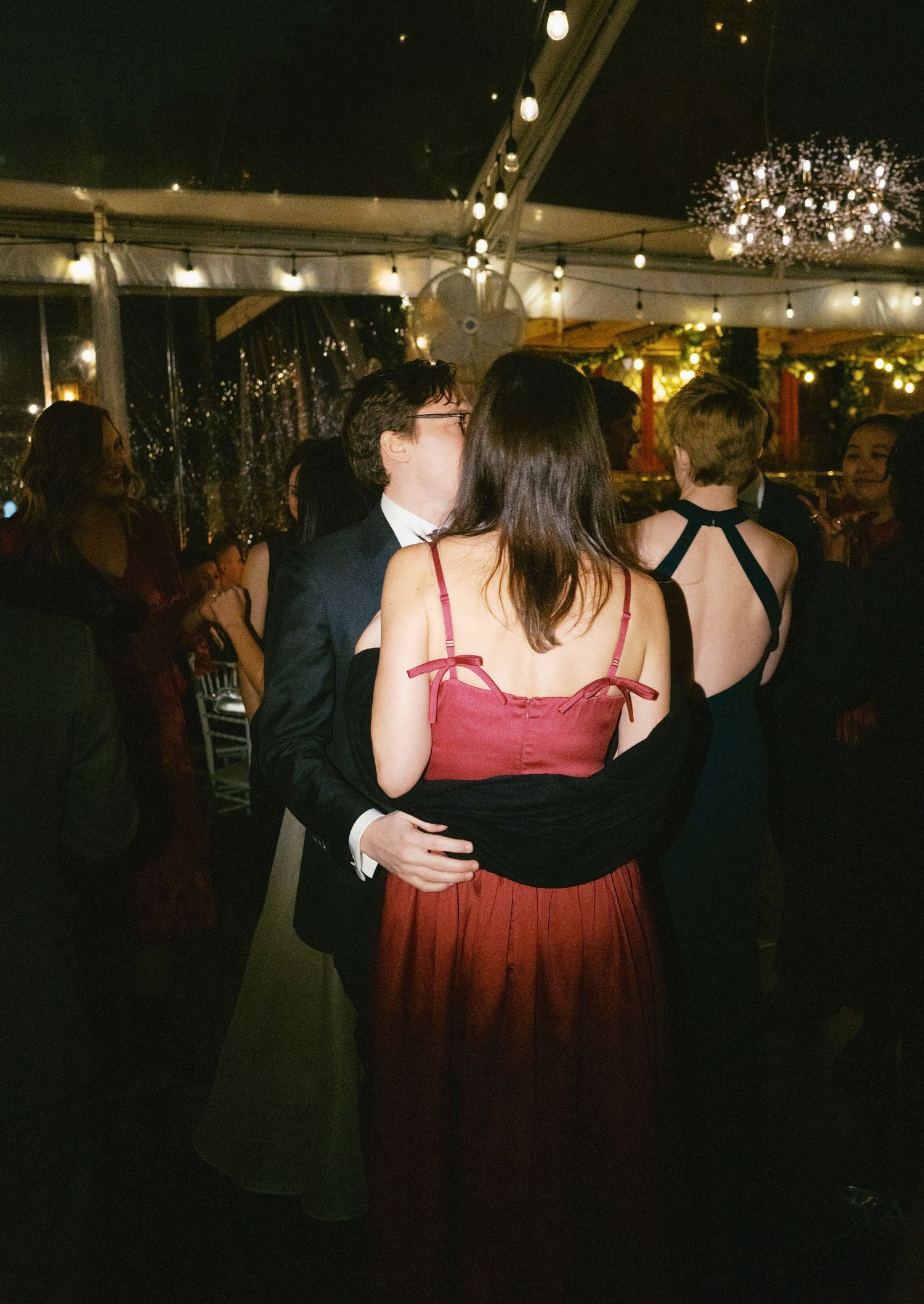 People dancing together at an evening wedding reception under twinkling lights and tent canopy.