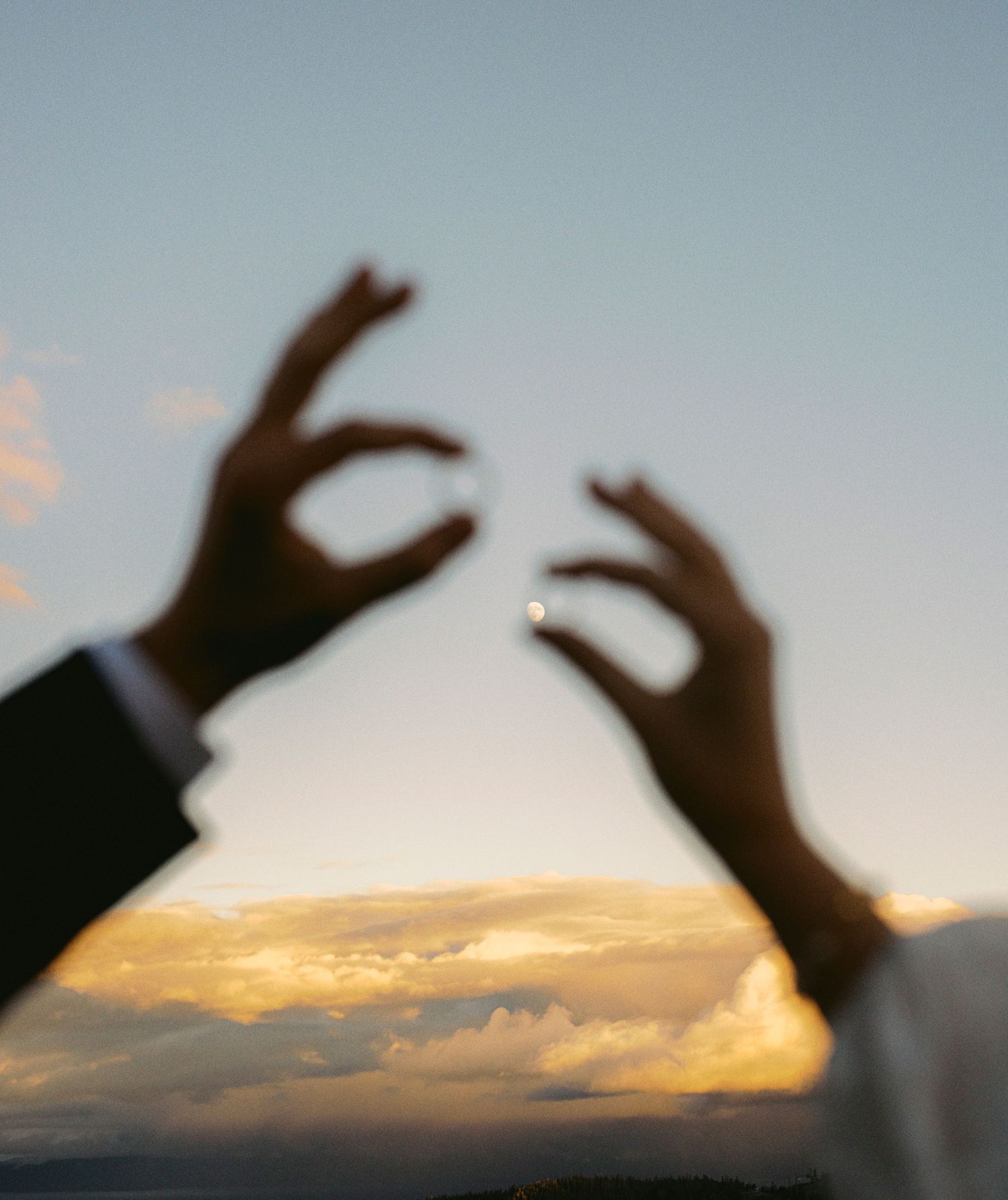 A sequence of silhouetted hands making heart shapes against a sunset sky with golden clouds.