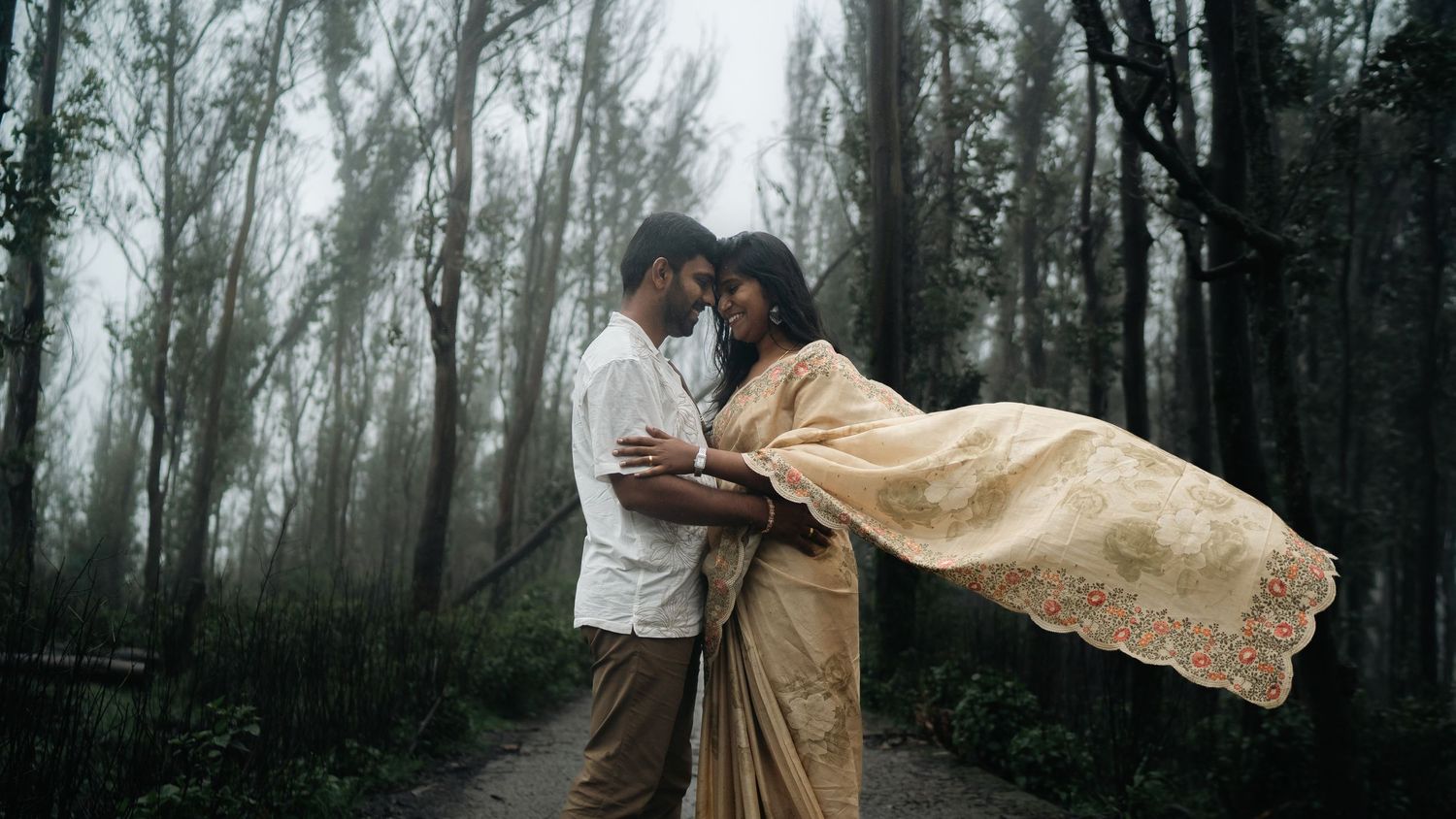A romantic moment in a misty forest with flowing fabric creating movement.