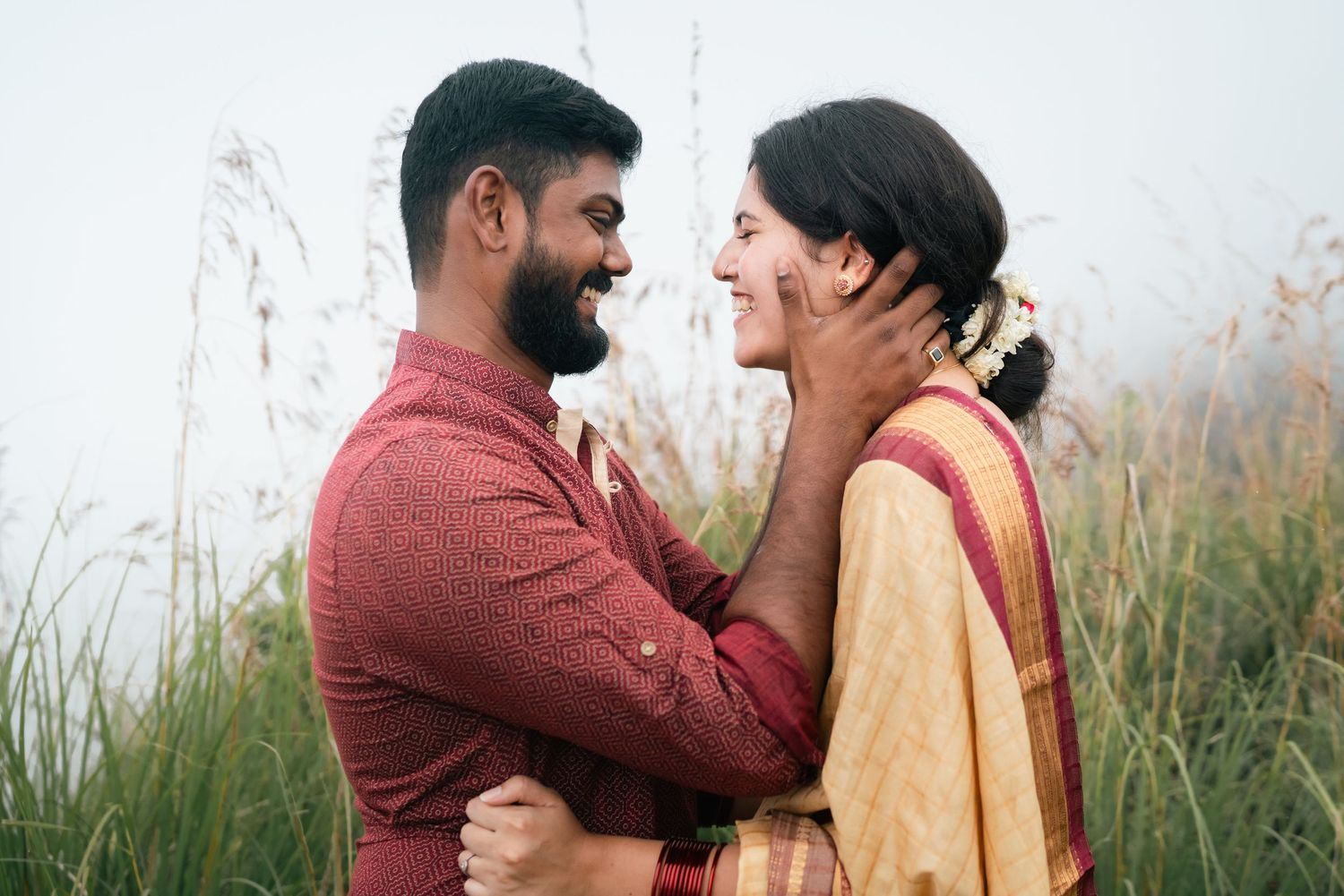 A joyful couple shares an intimate moment embracing in a field with tall grass.